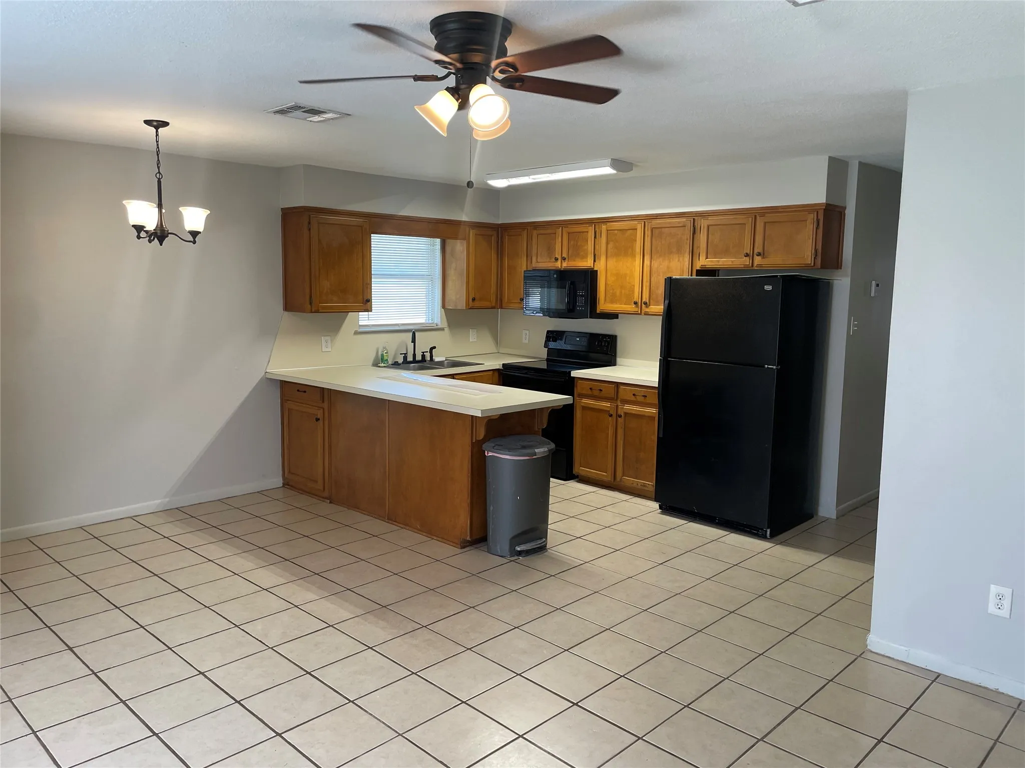 Kitchen featuring wood finish cabinetry, light countertops, black appliances, a peninsula, and ceiling fan