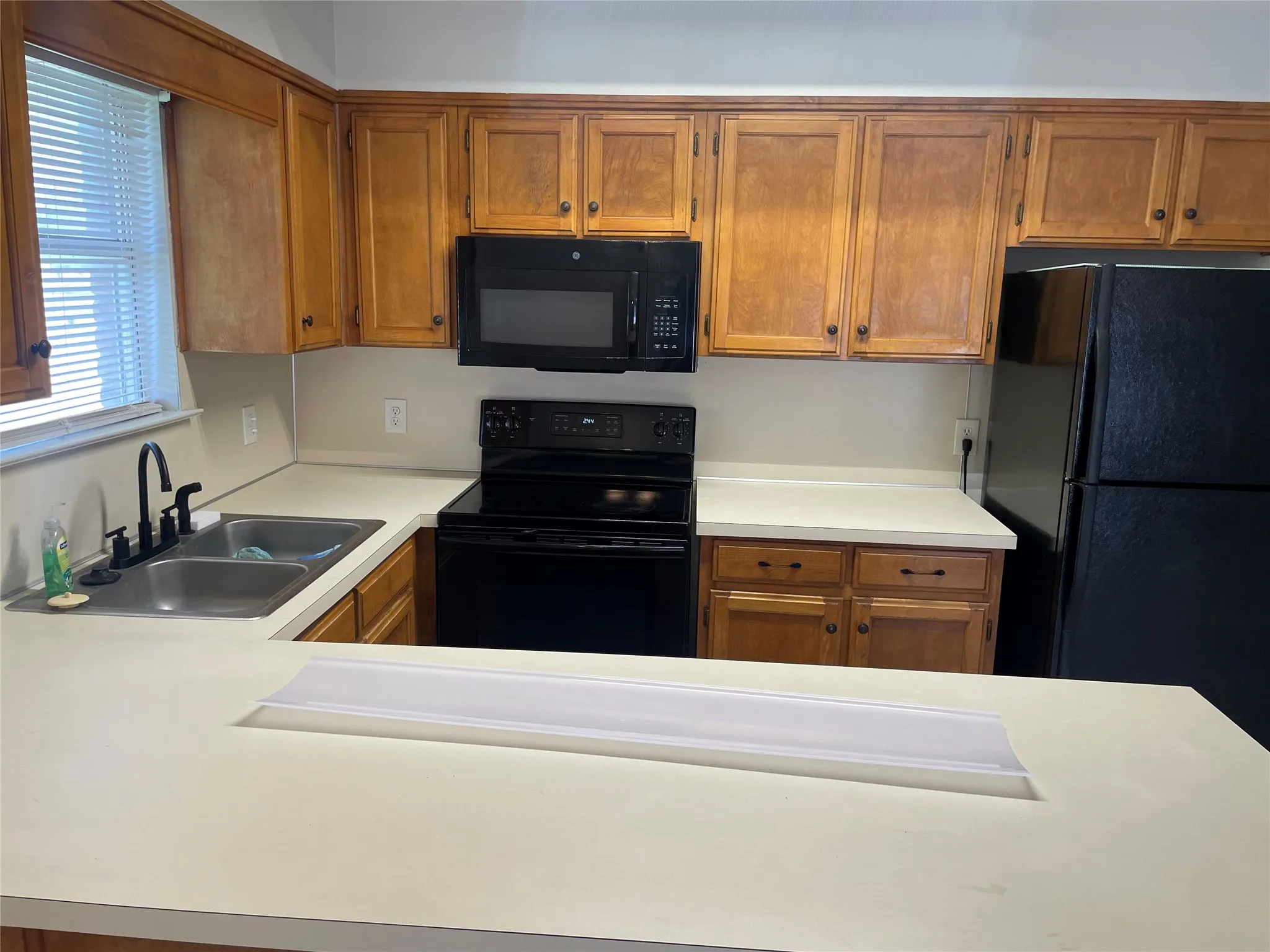 Kitchen with black appliances, wood finish cabinetry, and light countertops