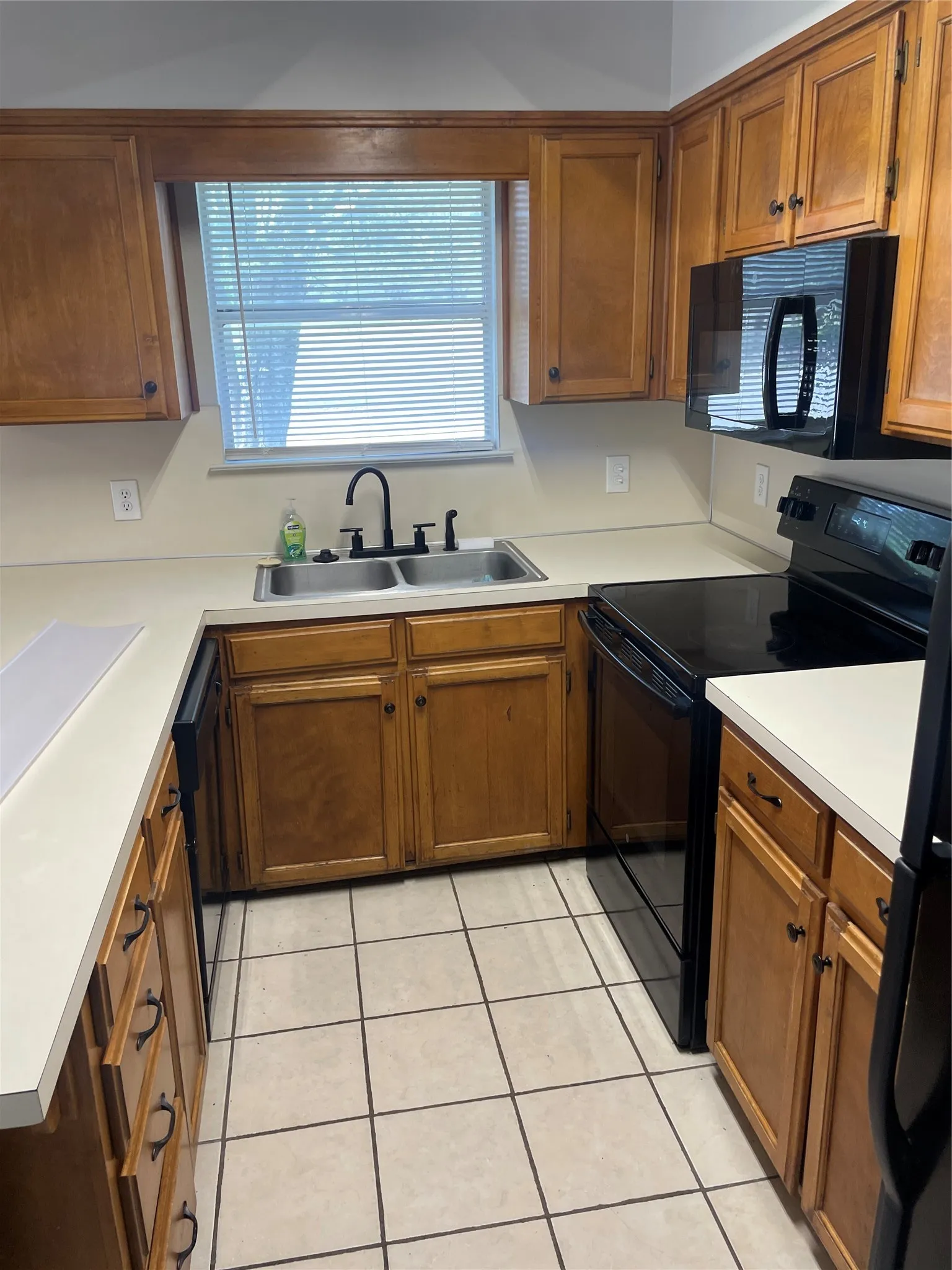 Kitchen featuring black appliances, wood finish cabinetry, light countertops, and light tile patterned floors