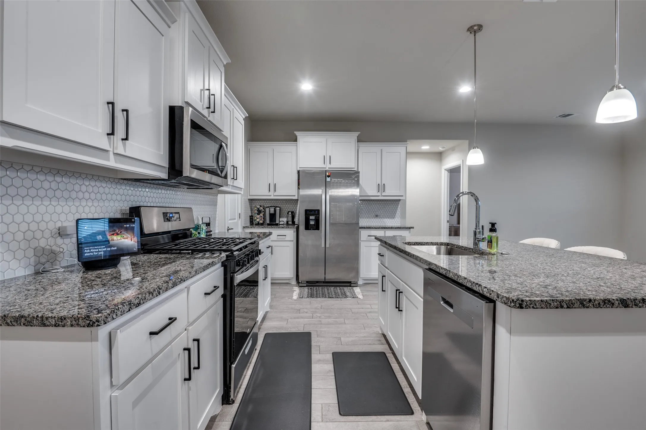 Kitchen with stainless steel appliances, dark stone countertops, white cabinetry, tasteful backsplash, and a kitchen island with sink