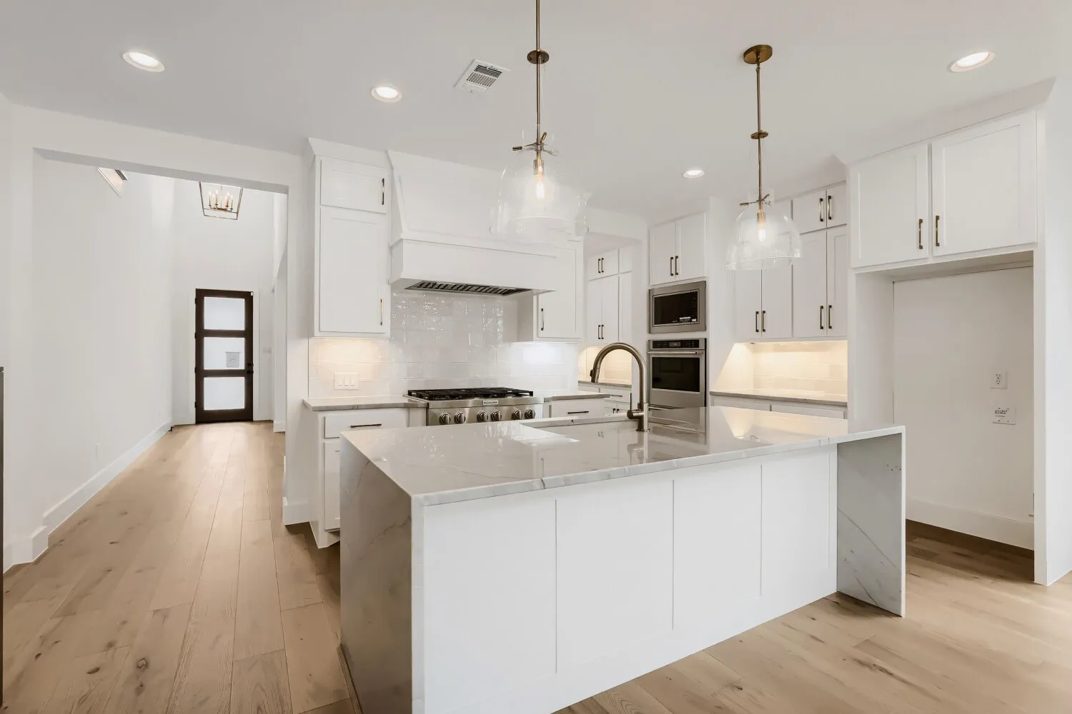 White kitchen cabinetry with integrated double ovens, a center island featuring a waterfall countertop, wood-finish flooring, and pendant lighting