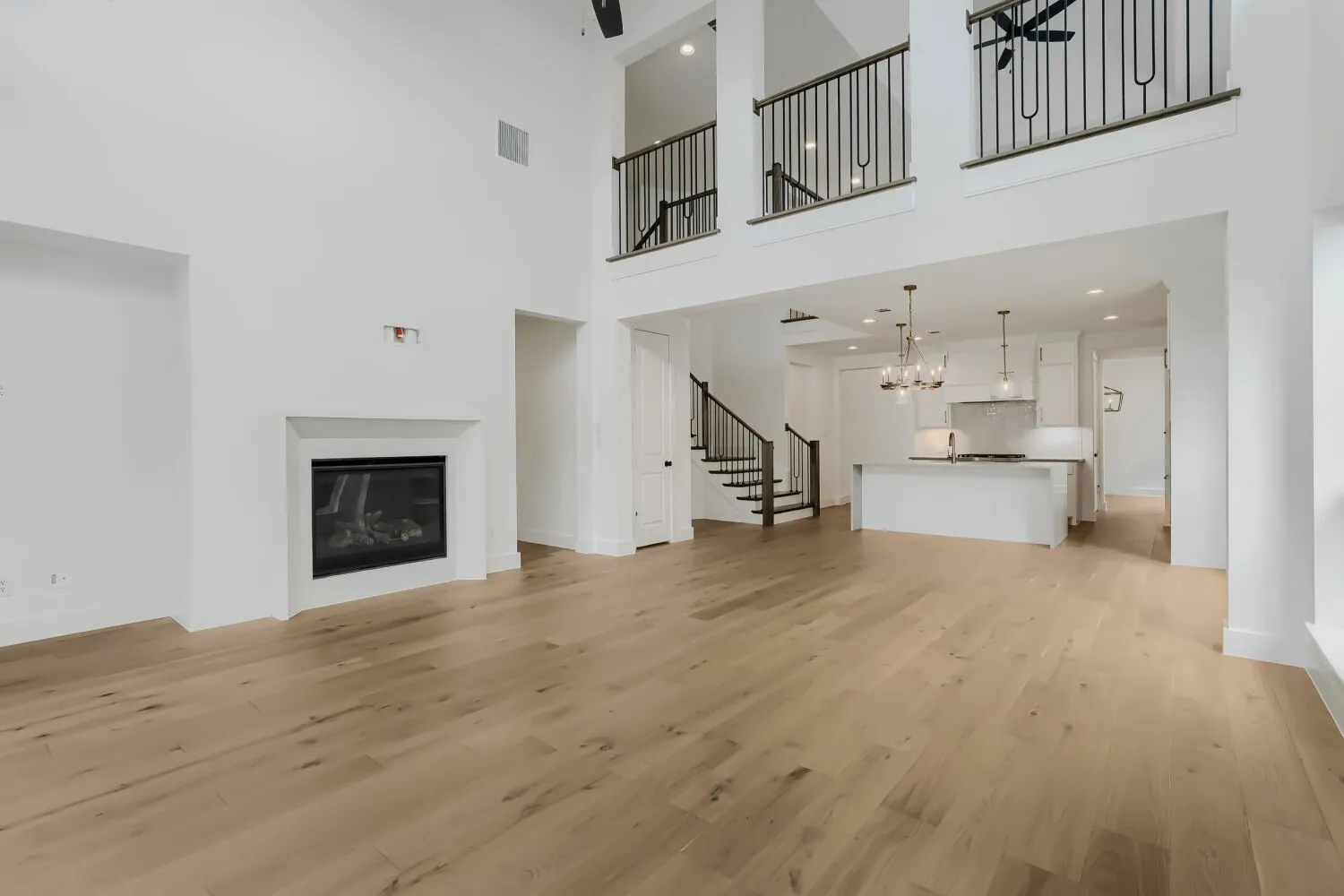 Hardwood flooring throughout, a gas fireplace with a white surround, and a kitchen island featuring pendant lighting