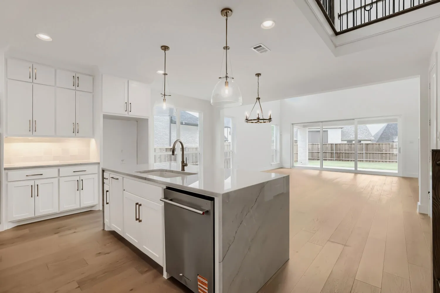 Modern kitchen featuring white cabinetry, a large center island with a waterfall countertop, stainless steel dishwasher, and wood-finish flooring