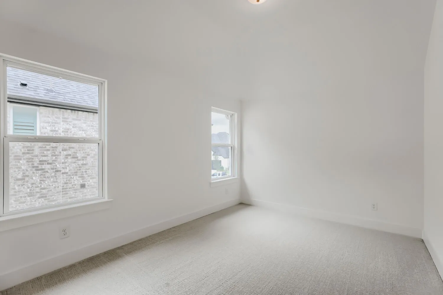 White walls with two windows, light-colored carpeting, and a ceiling-mounted light fixture