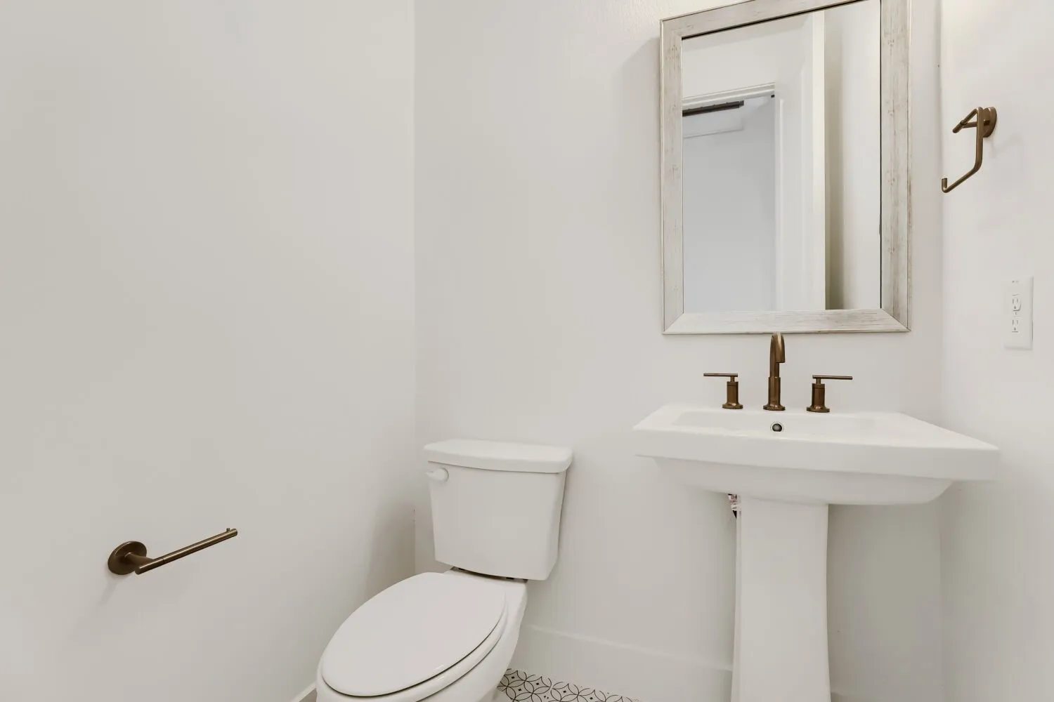Pedestal sink with bronze-finish faucet, framed wall mirror, and patterned floor tile
