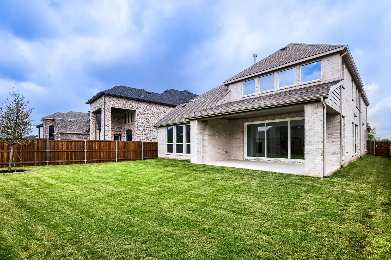 Expansive lawn area, covered patio, sliding glass doors, white brick exterior, dormer windows