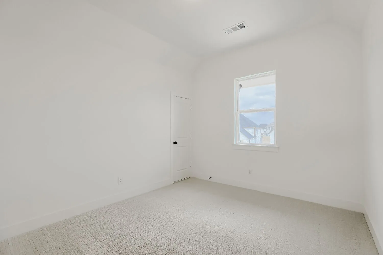 White painted walls, light-colored carpet flooring, single window, and a white door with black hardware