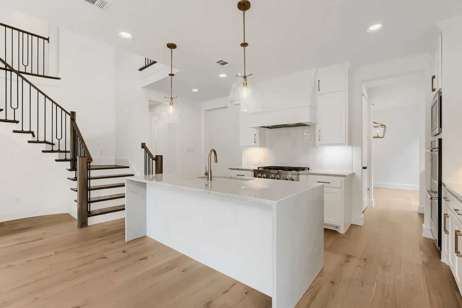 Gourmet kitchen with a large central island, white cabinetry, integrated range, and wall-mounted ovens