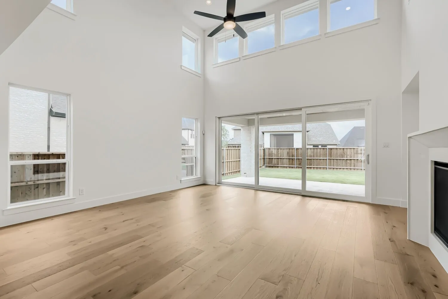 Two-story ceiling, wood-finish flooring, white walls, multiple windows, and sliding glass doors to the backyard