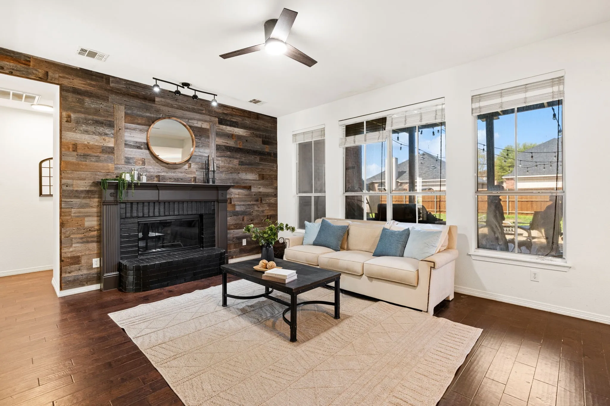 Living room with wooden walls, an accent wall, ceiling fan, a fireplace, and dark wood finished floors