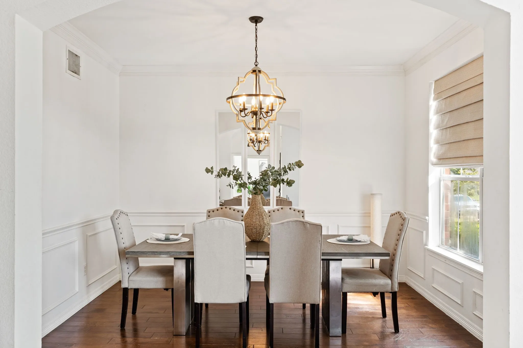 Dining room with ornamental molding, a decorative wall, arched walkways, wainscoting, and hanging lights