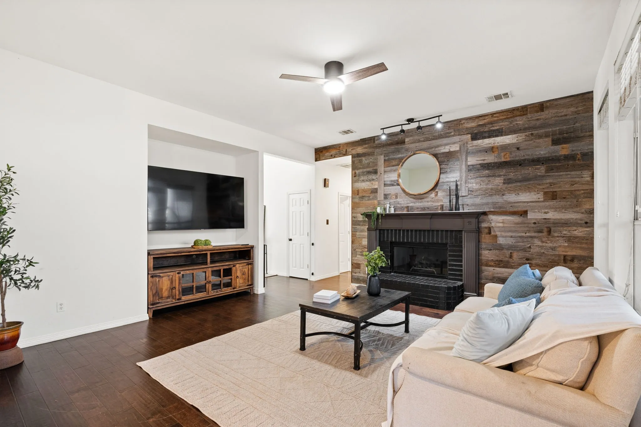 Living area with wood walls, a ceiling fan, track lighting, dark wood-type flooring, and a fireplace