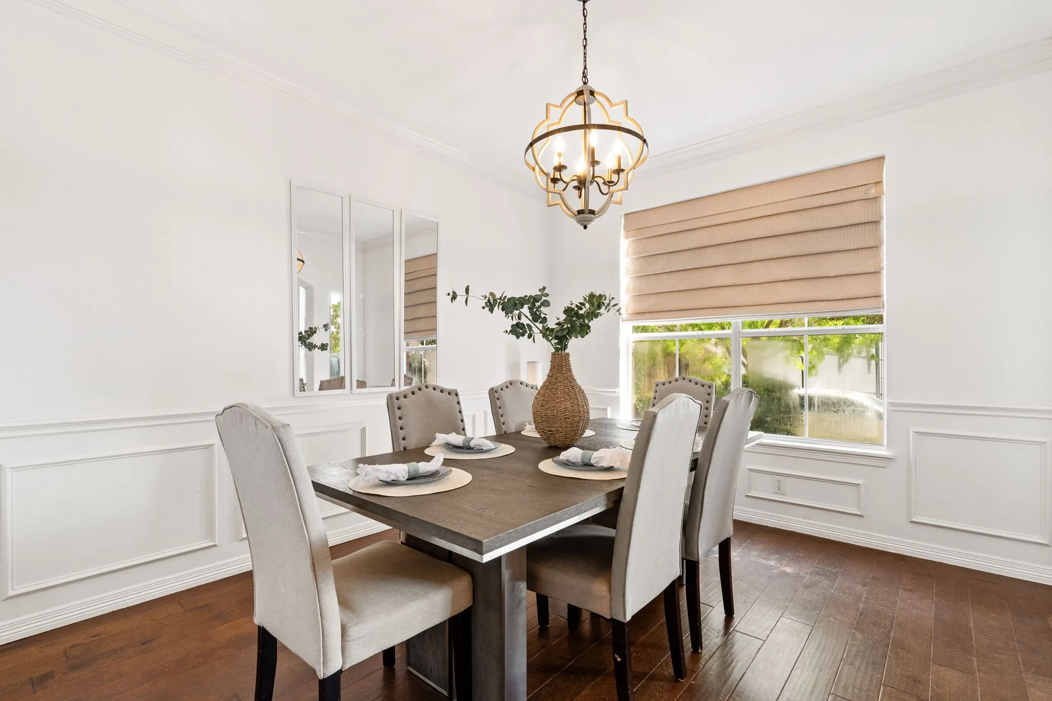 Dining room featuring ornamental molding, a wainscoted wall, a decorative wall, hanging lights, and dark wood finished floors