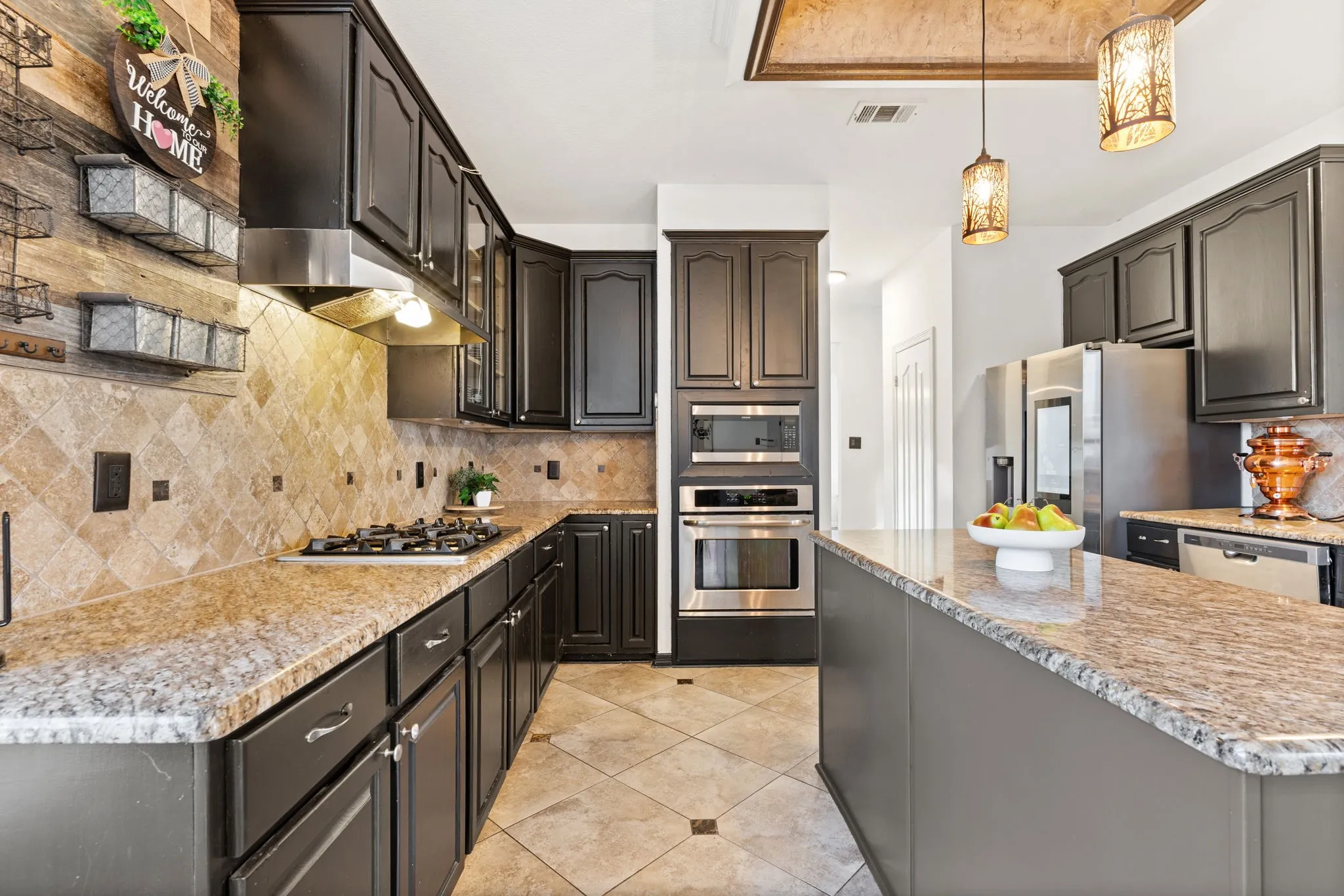 Kitchen featuring stainless steel appliances, hanging light fixtures, light stone counters, and decorative backsplash