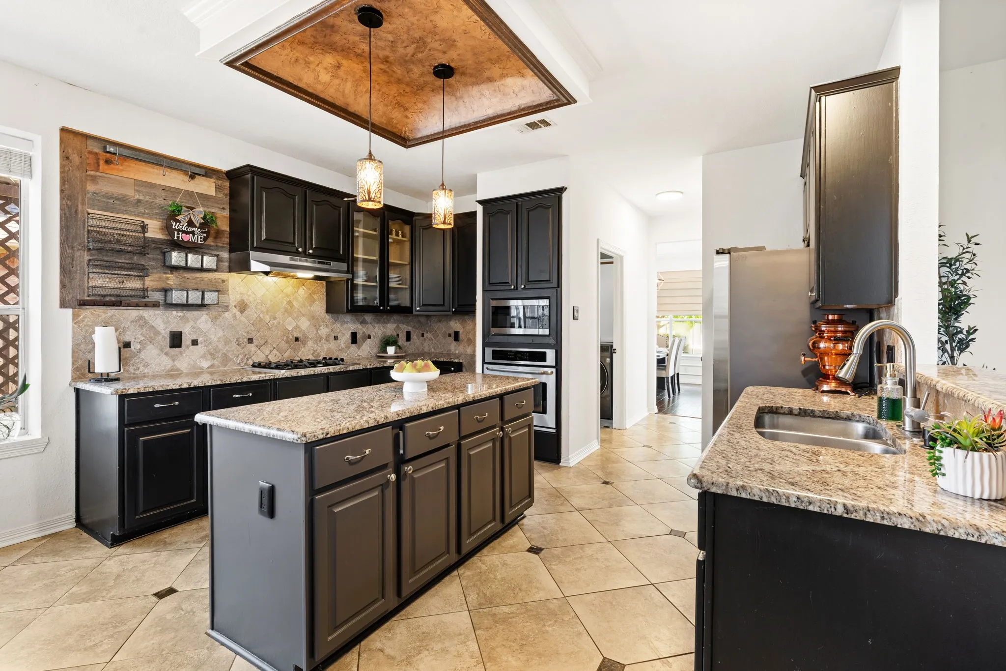 Kitchen featuring a kitchen island, light stone countertops, dark cabinetry, pendant lighting, and light tile patterned floors