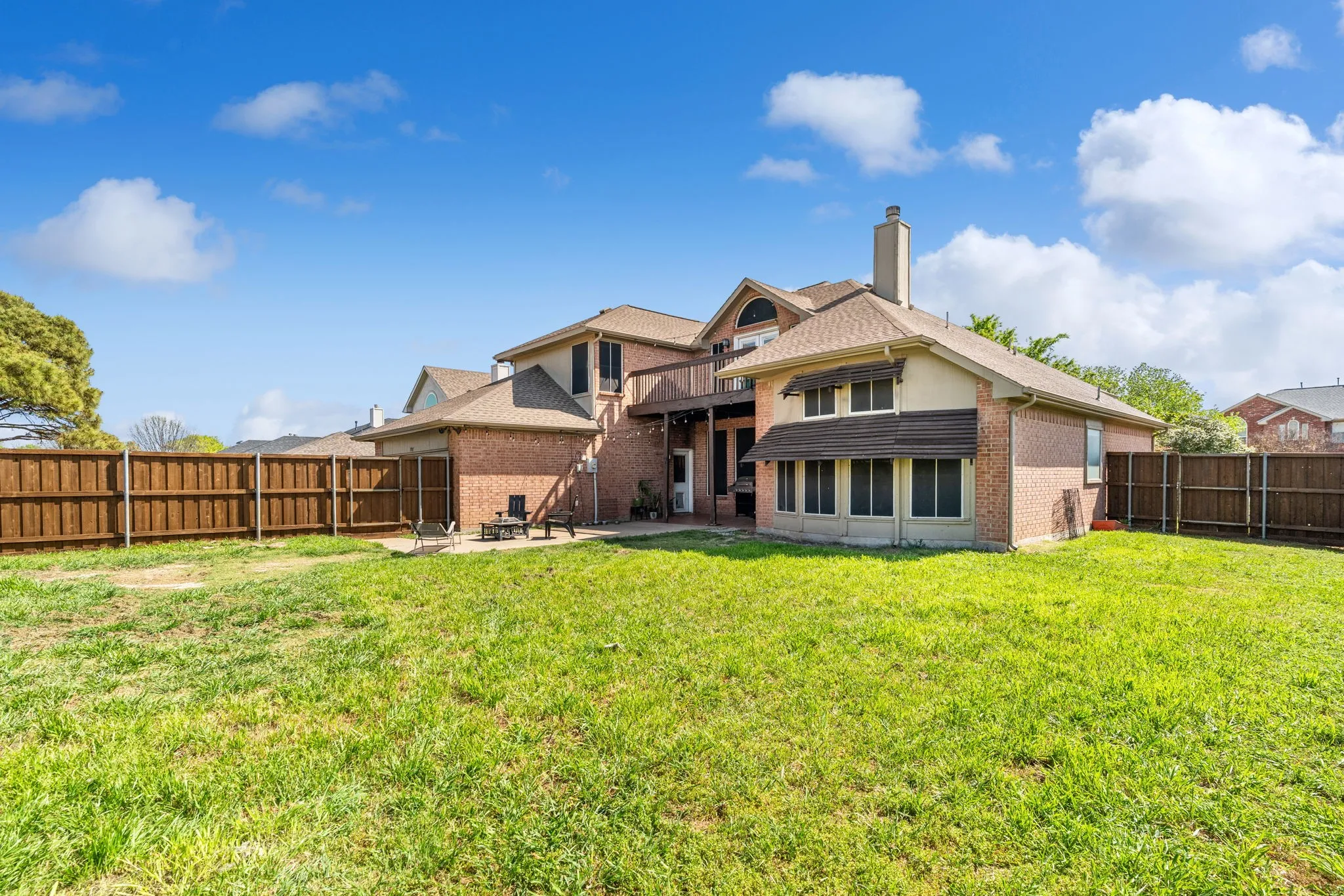 Back of house with brick siding, a chimney, a fenced backyard, a patio area, and roof with shingles