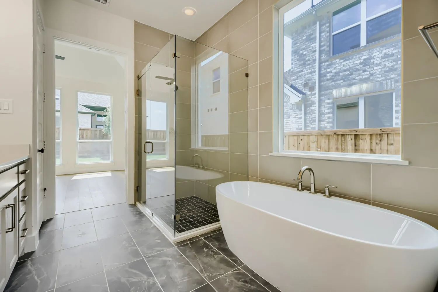 Bathroom featuring a freestanding soaking tub with deck-mounted fixtures, a glass-enclosed shower with a dark tile floor, and a large window