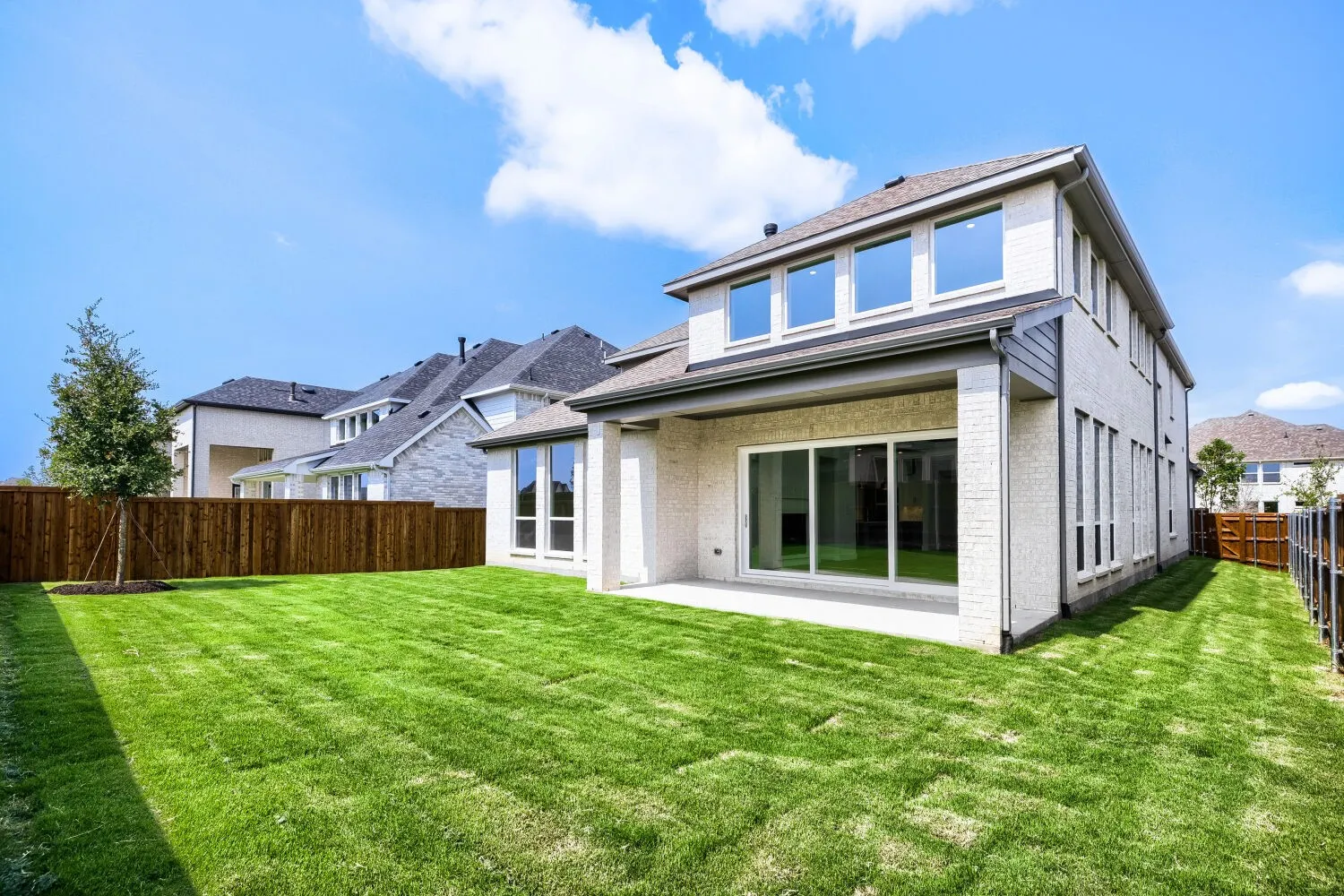 Expansive backyard featuring a lush lawn, privacy fencing, and a covered patio area