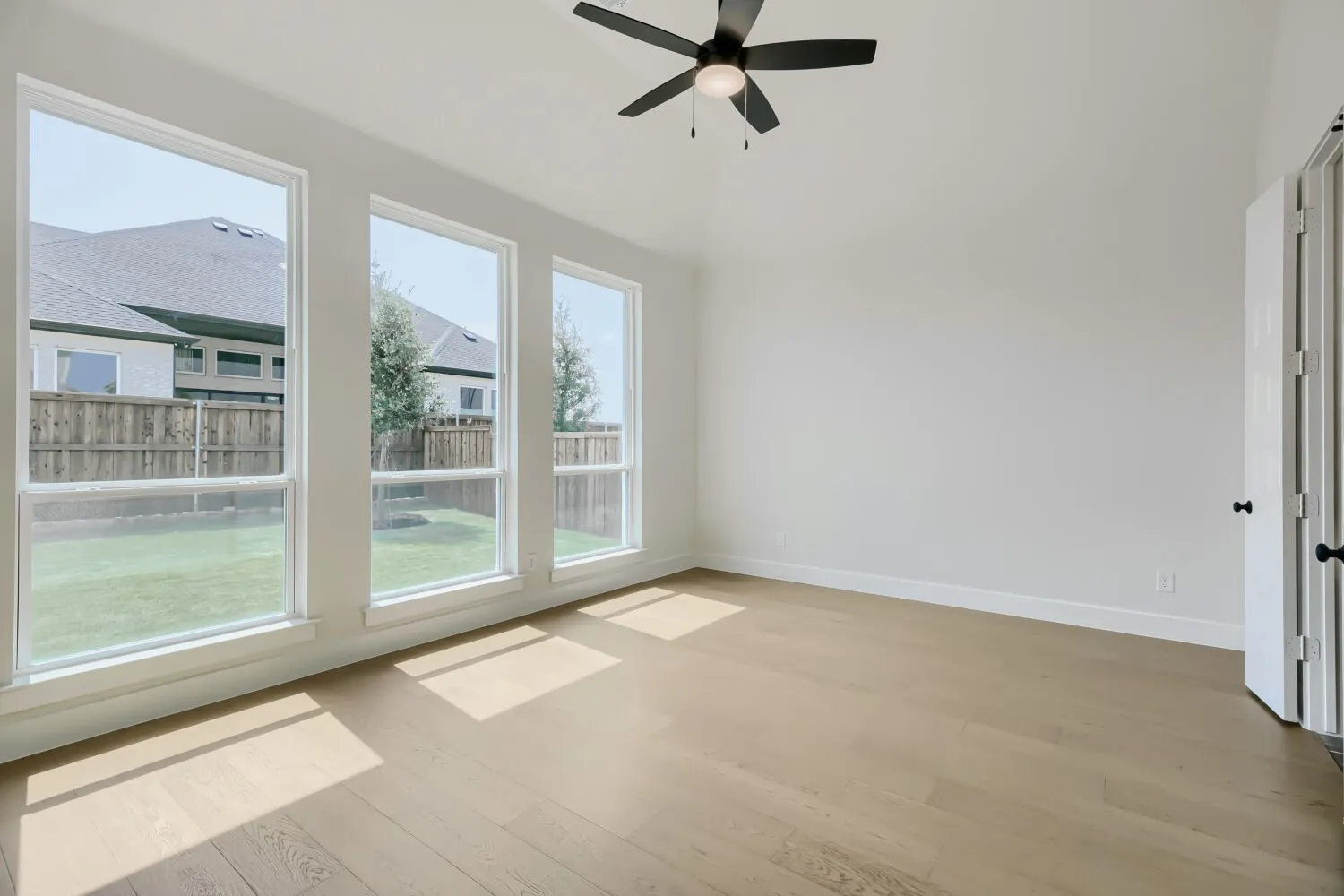 Room featuring light wood-finish flooring, three large windows, a vaulted ceiling, and a ceiling fan with integrated lighting