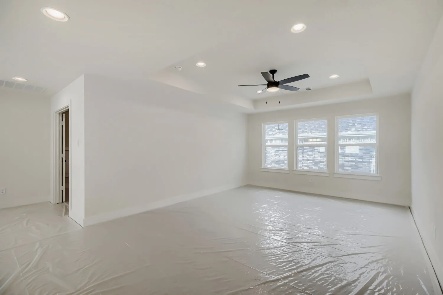 Spacious room featuring a tray ceiling with a ceiling fan, recessed lighting, and three large windows
