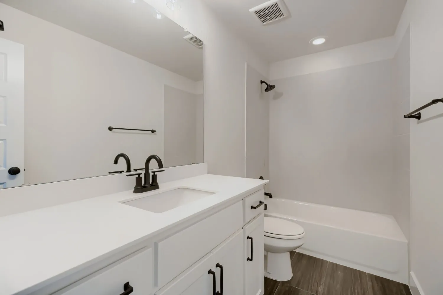 Bathroom featuring a white vanity with integrated sink and matte black faucet, full-width mirror, and a white bathtub with shower