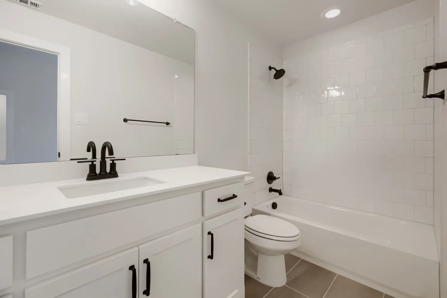 Contemporary bathroom featuring a white vanity with integrated sink, matte black fixtures, and a subway-tiled shower with tub