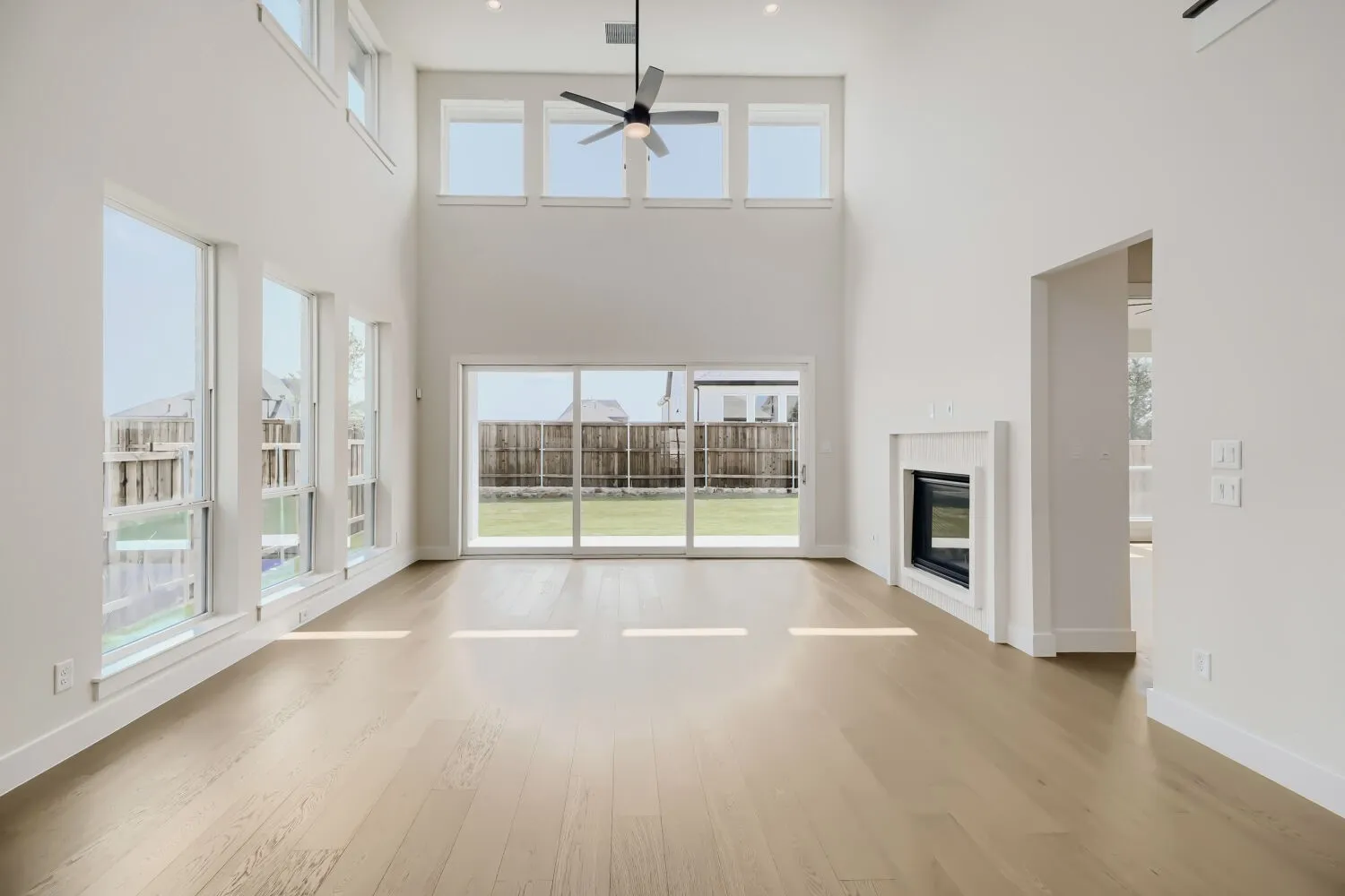 Two-story living area featuring wood-finish flooring, a contemporary fireplace, and a ceiling fan
