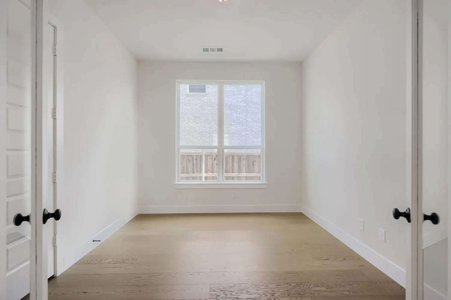 Bright room featuring light wood-finish flooring, white walls, and a large window with privacy shades