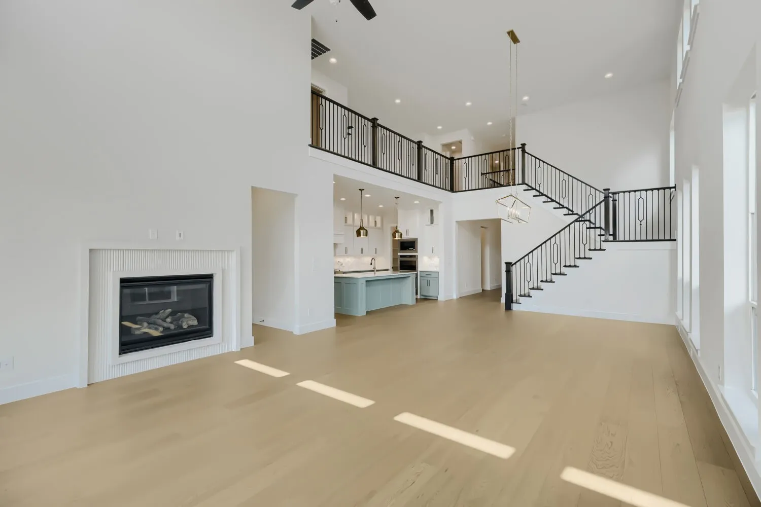 Spacious living area featuring light wood-finish flooring, a contemporary fireplace with white fluted tile surround, a double-height ceiling, and a prominent staircase with black metal railings