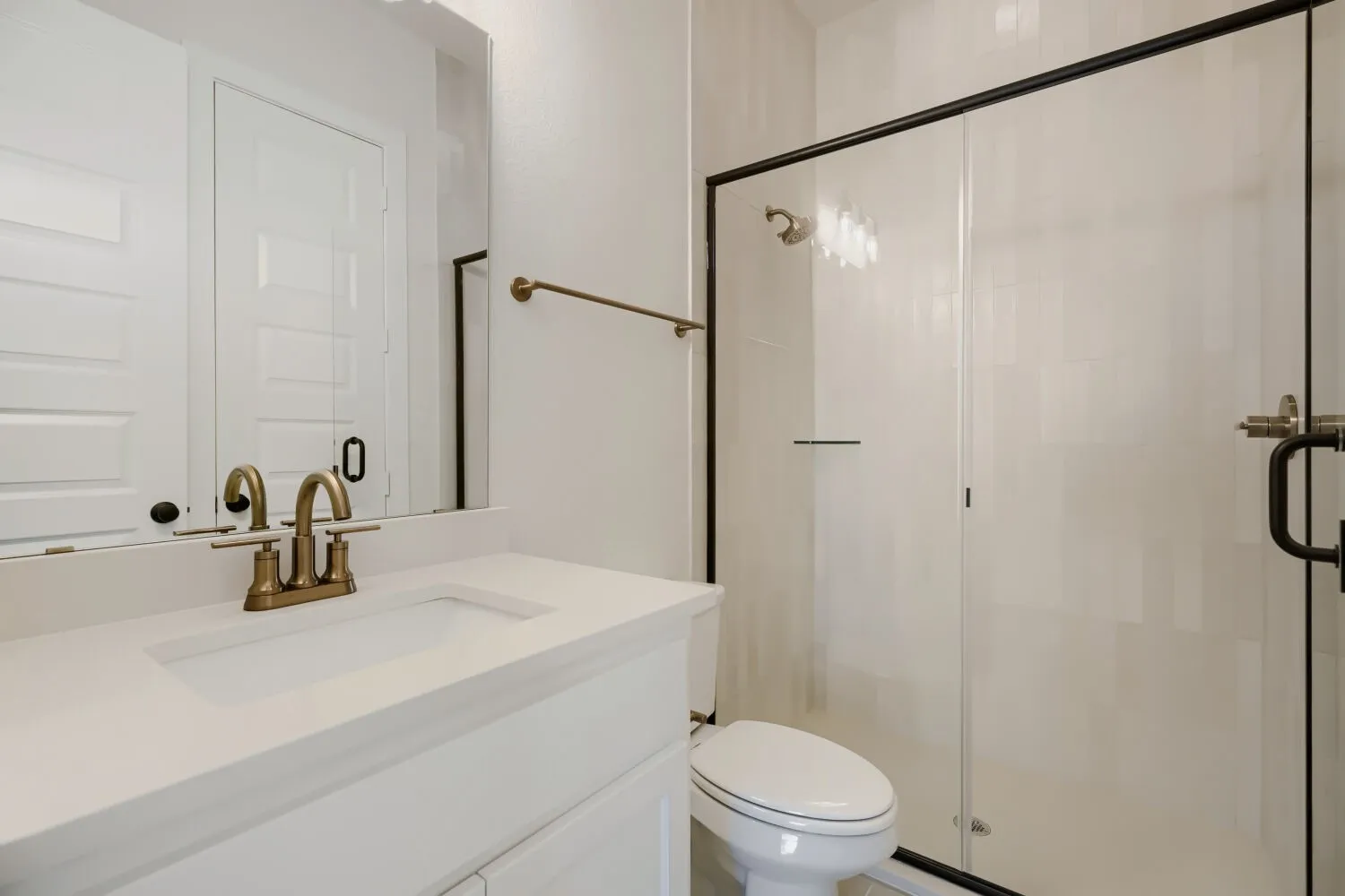Full bathroom featuring a white vanity with integrated sink, brass-finish faucet, and a frameless glass shower enclosure with black trim