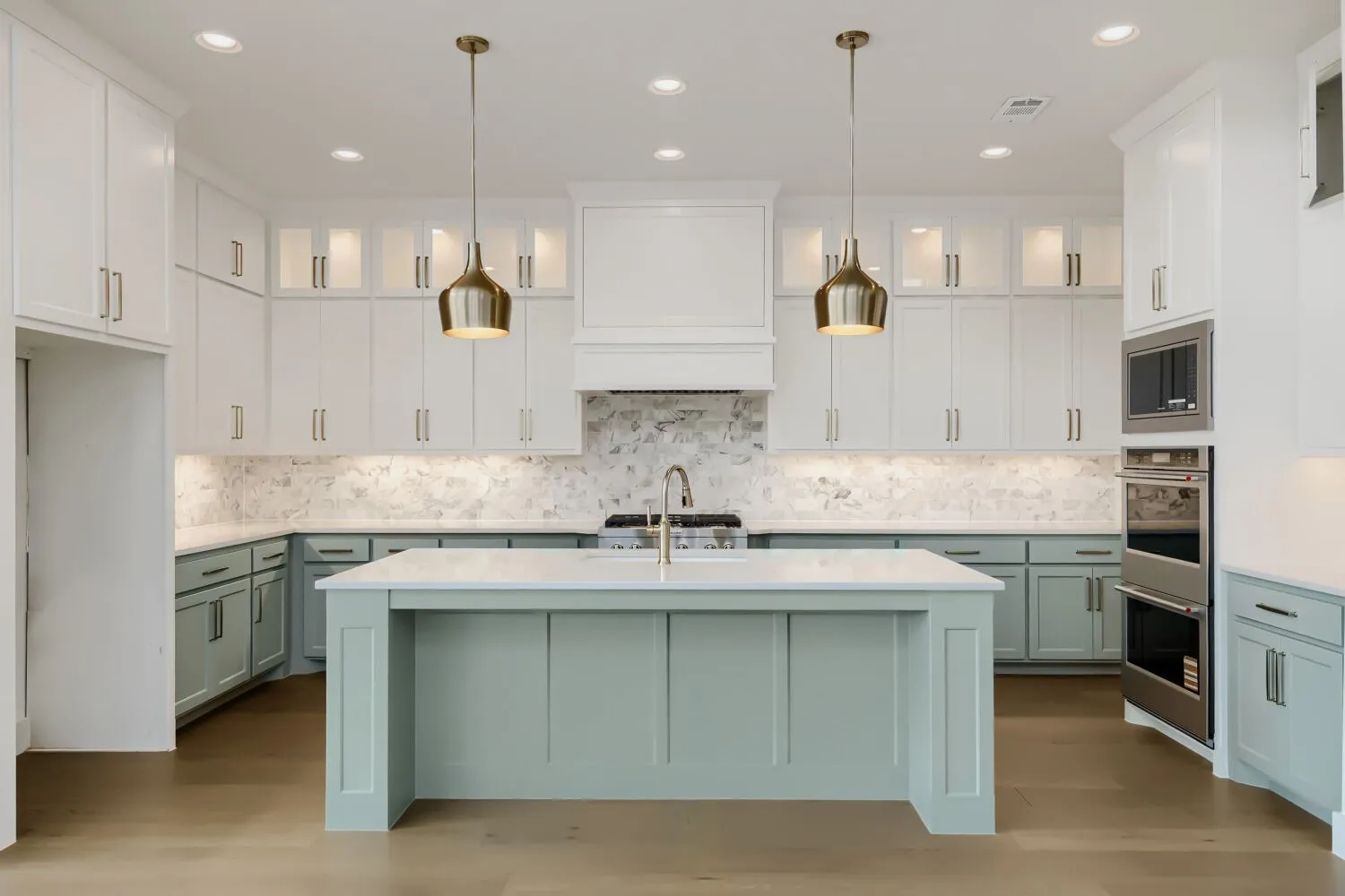 Spacious kitchen featuring a central island with a light-colored countertop, two-tone cabinetry, stainless steel double ovens, and recessed lighting