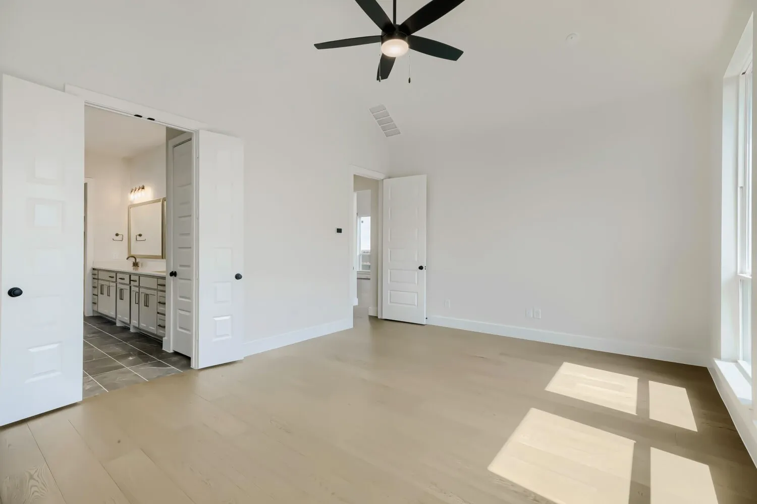 Spacious room featuring light wood-finish flooring, a vaulted ceiling, and an integrated ceiling fan