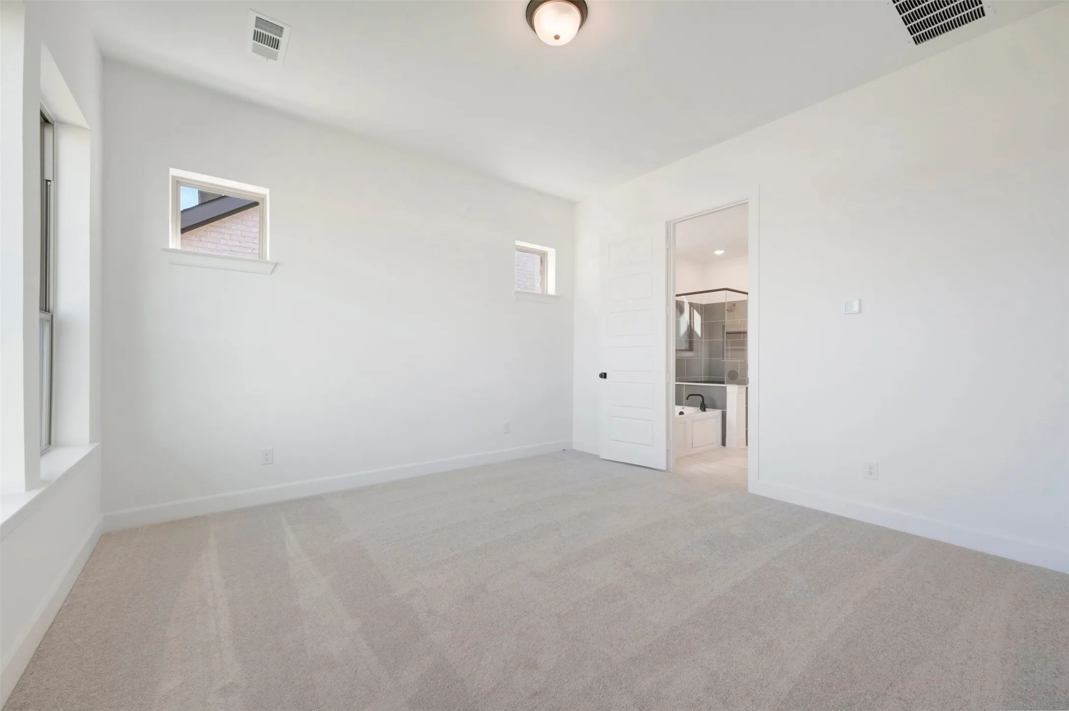 Spacious room featuring light-toned carpet flooring, white painted walls, and multiple windows