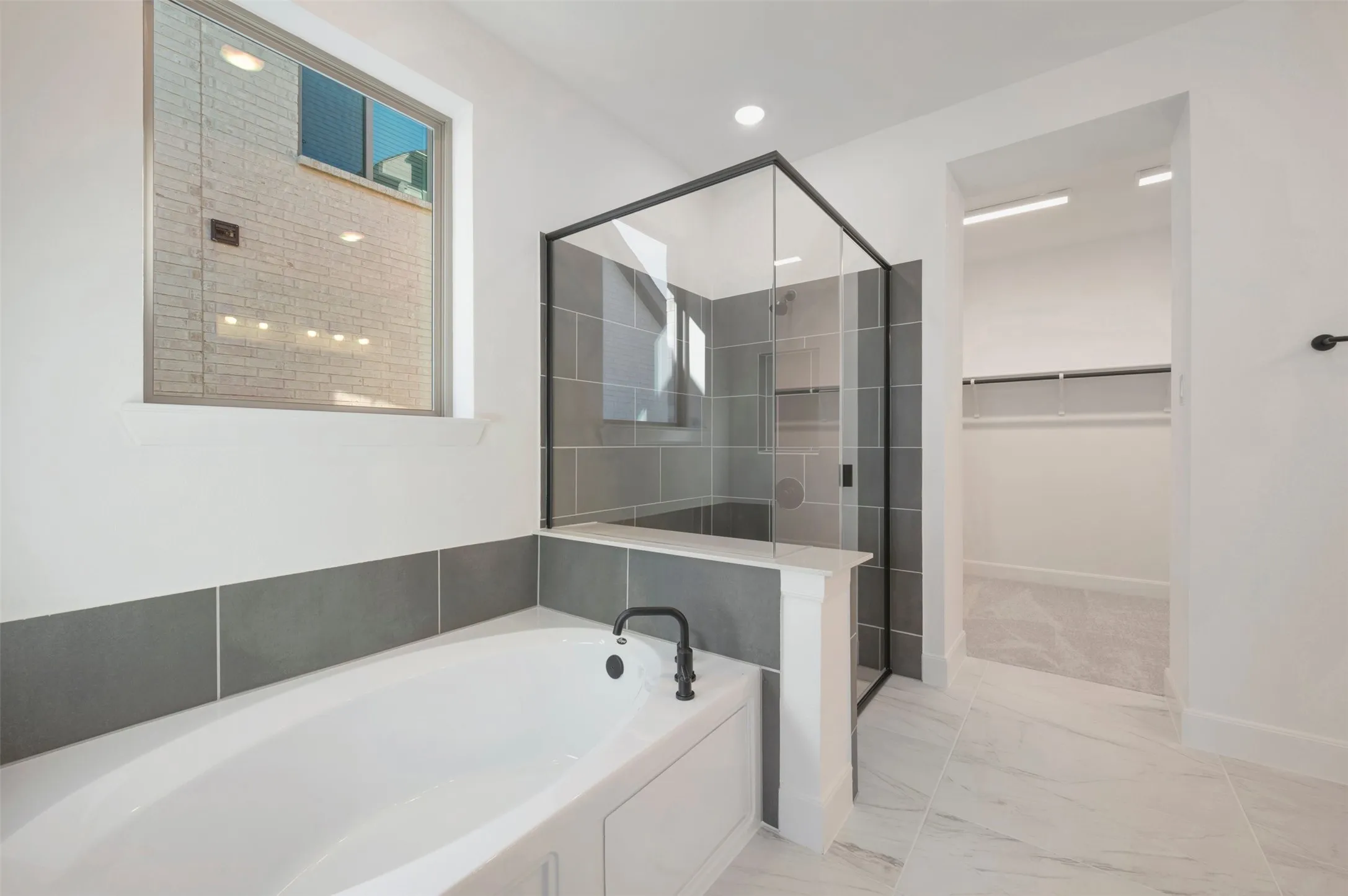 Modern bathroom featuring a built-in tub with matte black fixtures, a glass-enclosed shower with subway tile surround, and large format marble-look floor tiles