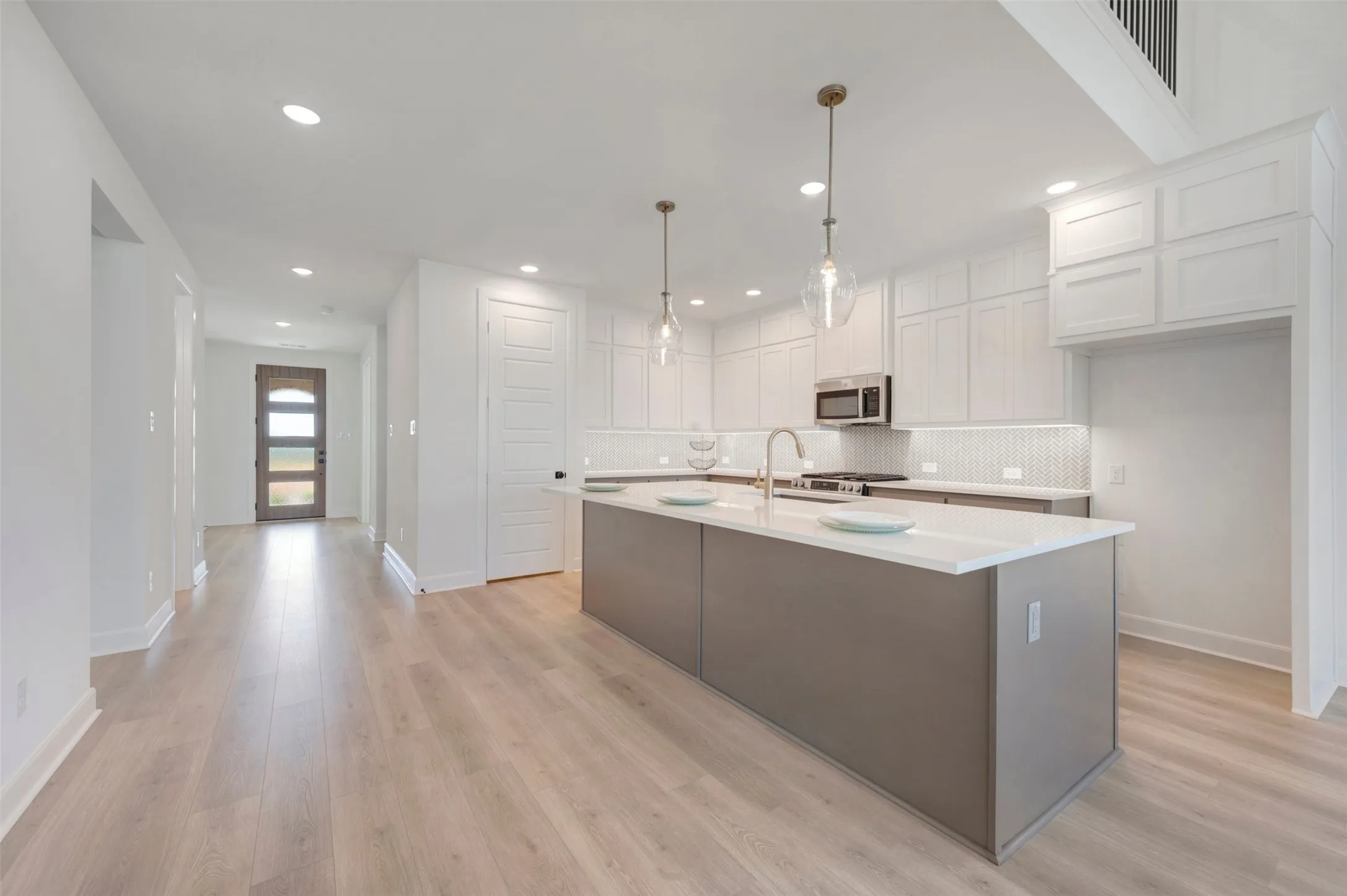 Open-concept kitchen featuring an expansive island with a white countertop, stainless steel appliances, white cabinetry, and wood-finish flooring