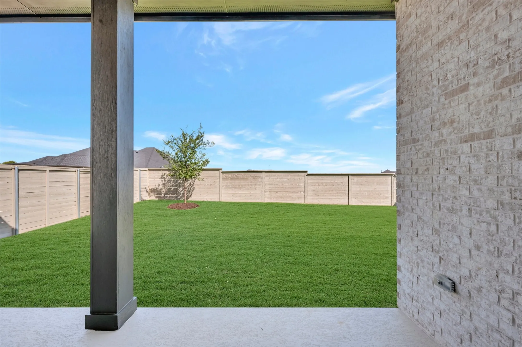 Expansive backyard featuring a manicured lawn, established tree, and full perimeter fencing