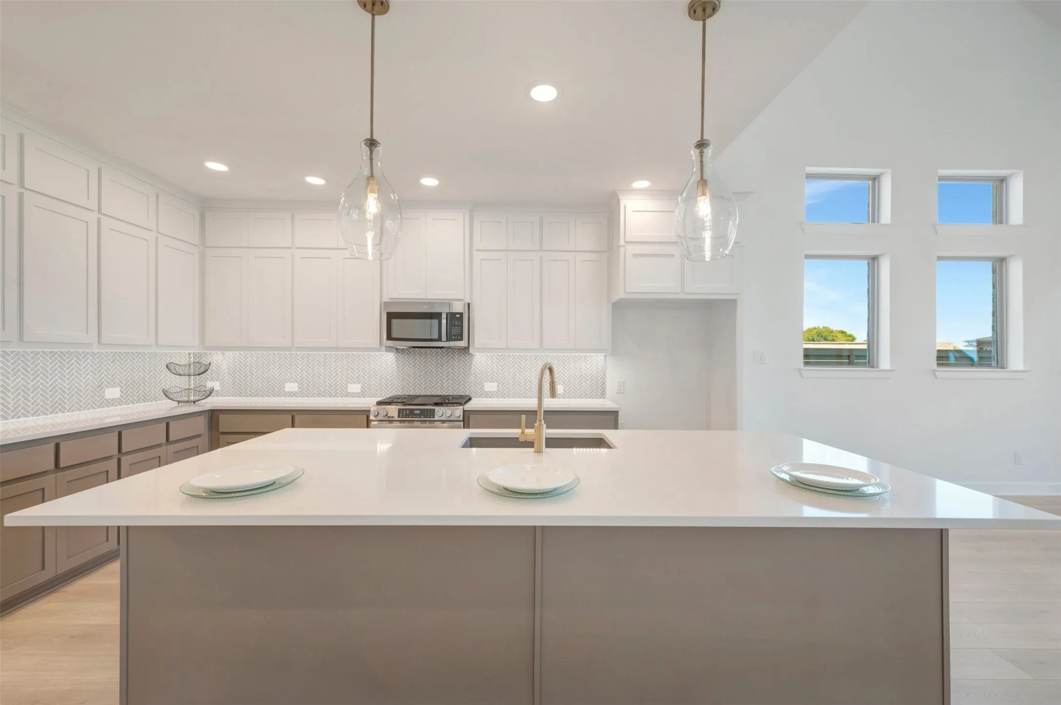 Kitchen featuring a large center island with a sink, white shaker-style upper cabinetry, contrasting lower cabinetry, a herringbone tile backsplash, and stainless steel appliances