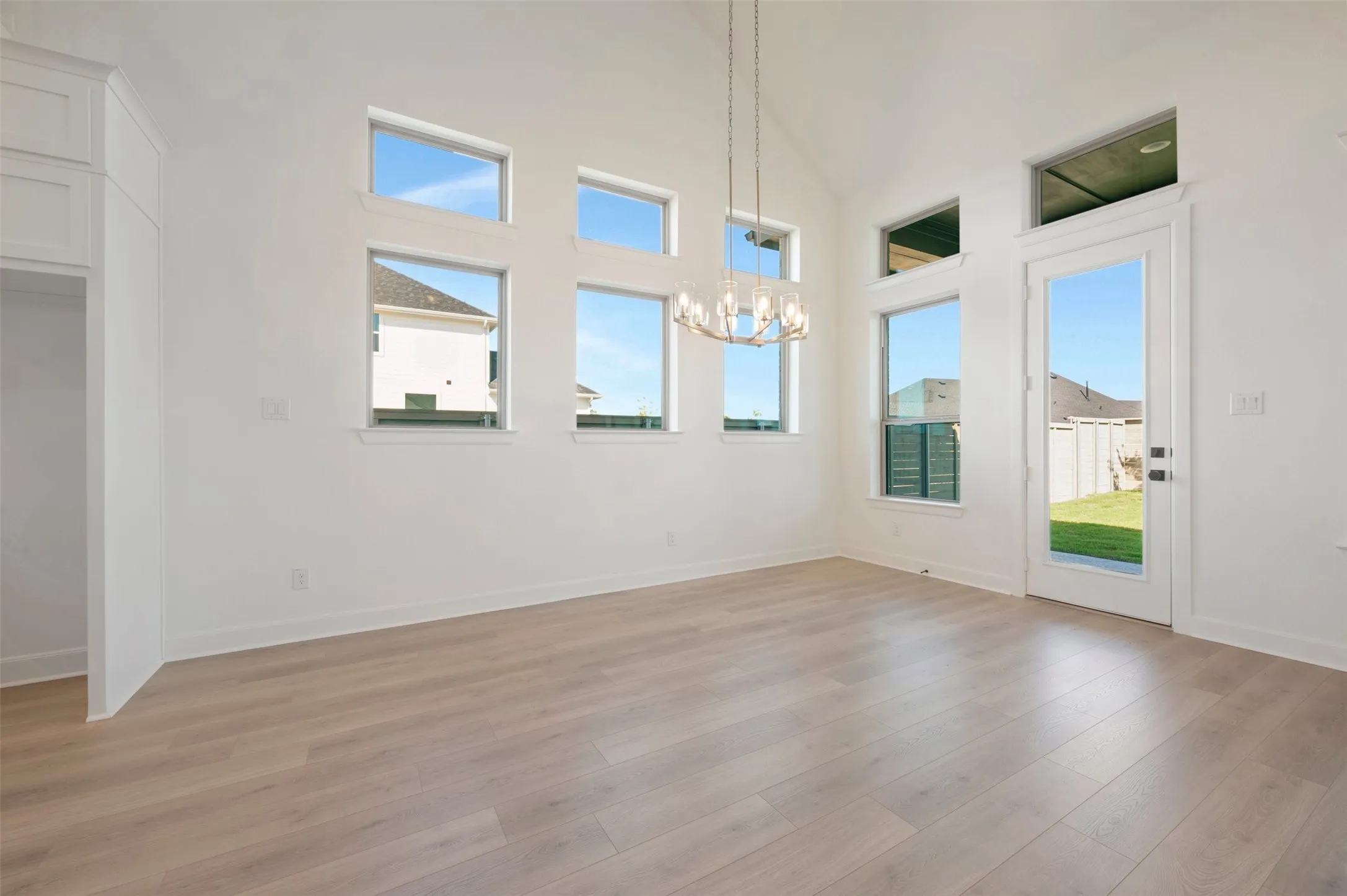 Vaulted ceiling with a contemporary chandelier, multiple transom windows, wood-finish flooring, and a glass-paneled exterior door