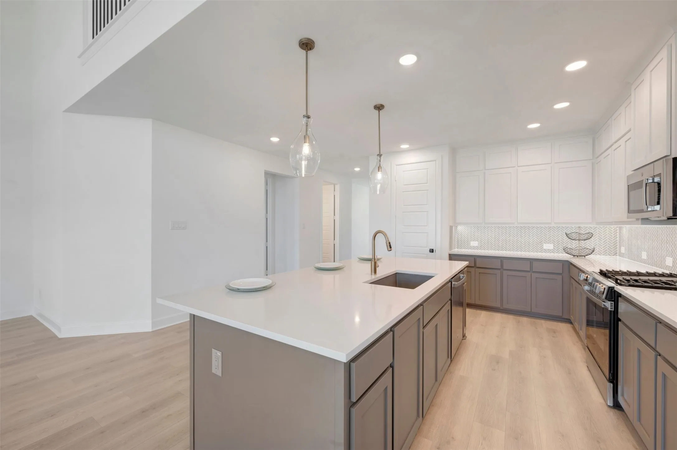Modern kitchen with a large central island, white countertops, two-tone cabinetry, stainless steel appliances, and wood-finish flooring