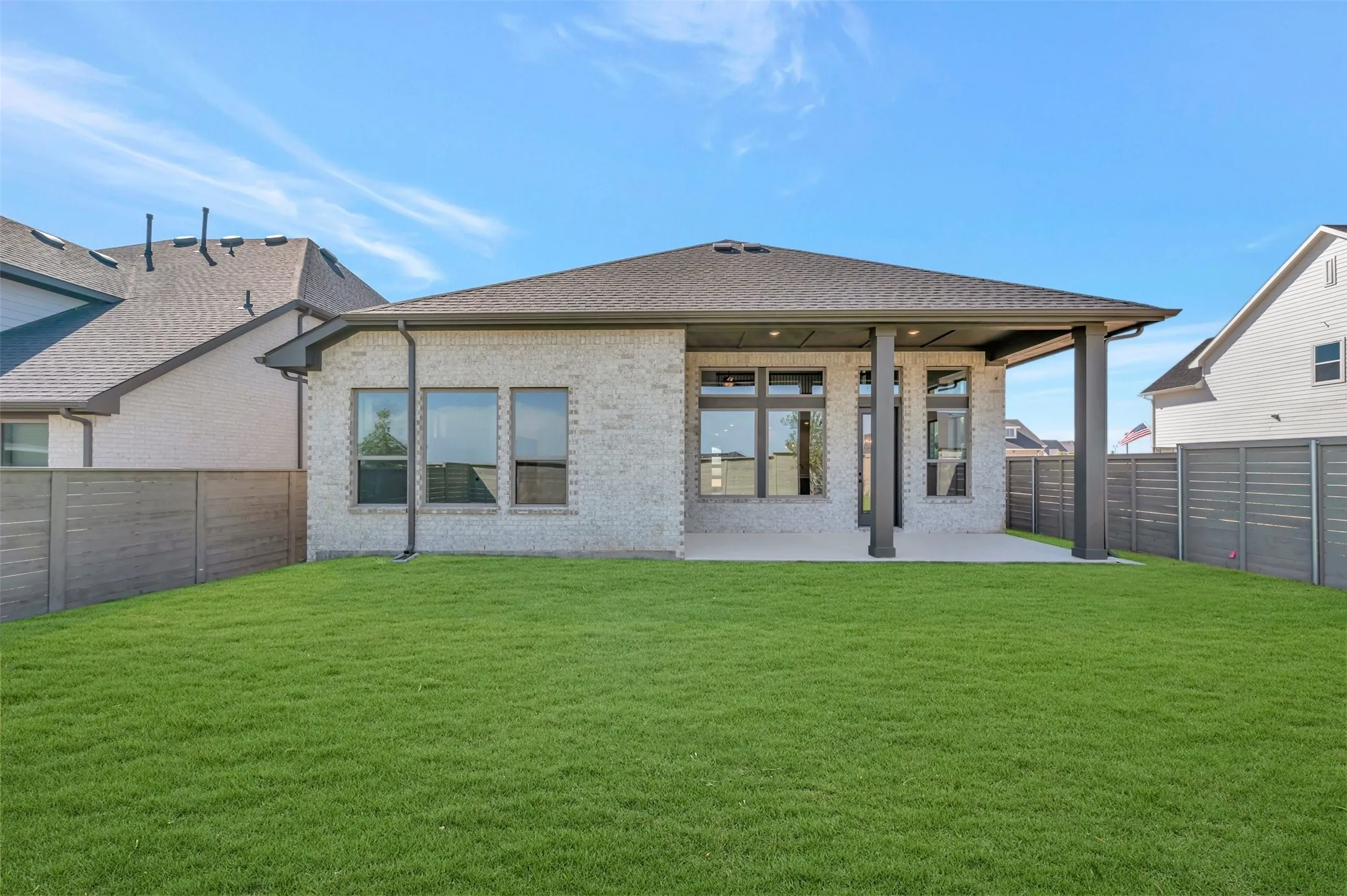 Expansive green lawn with a covered concrete patio featuring dark support pillars