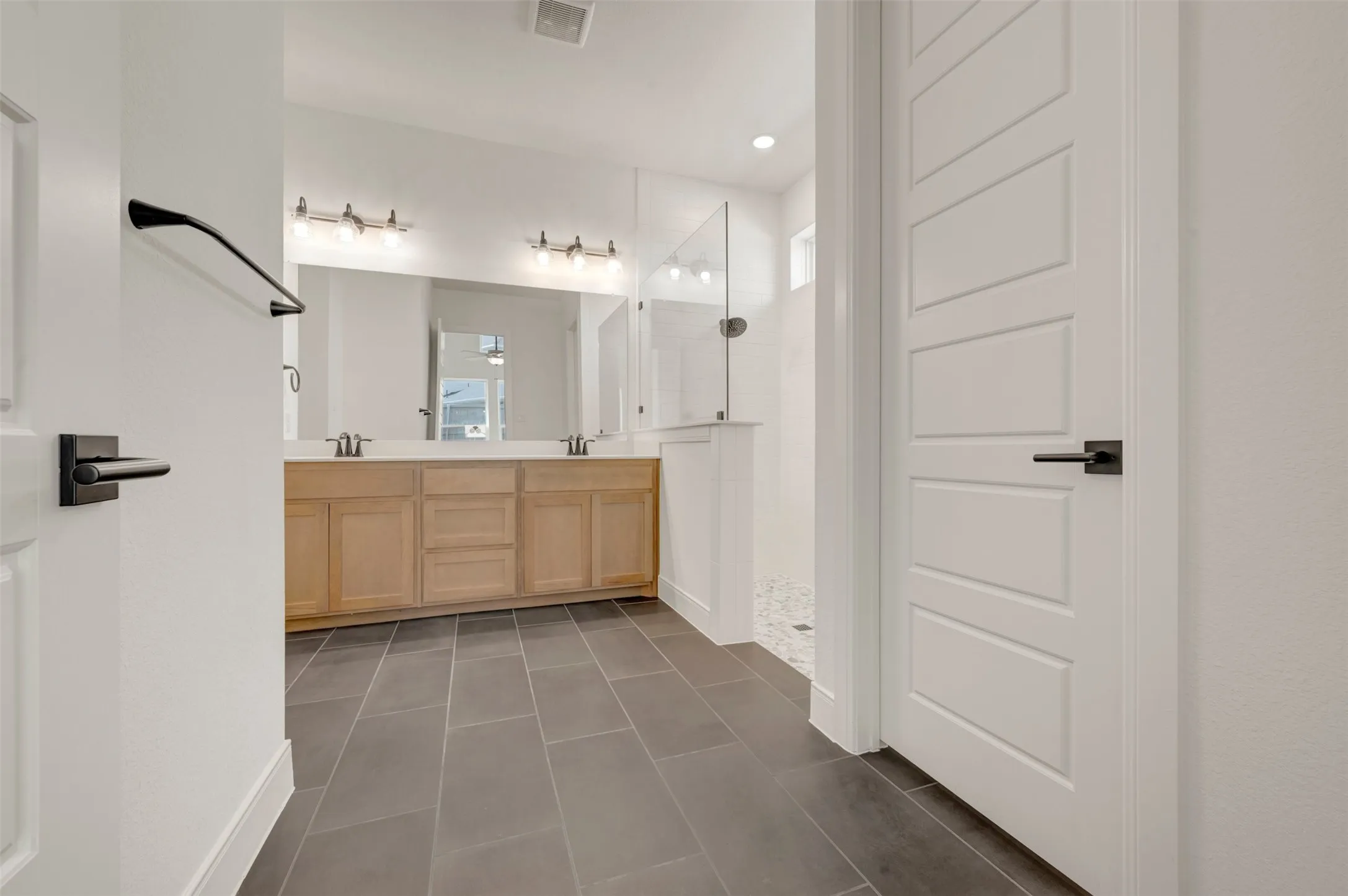 Spacious bathroom featuring a dual vanity with light wood cabinetry, a large frameless mirror, and modern light fixtures