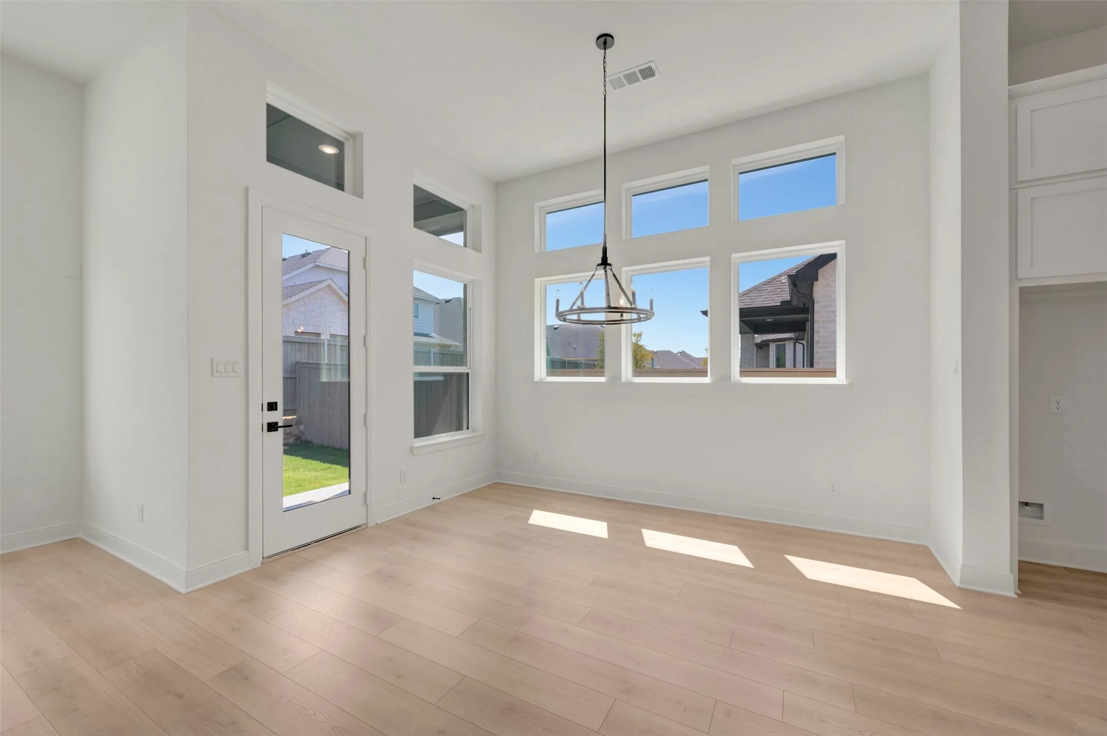 Spacious room featuring light wood-finish flooring, a contemporary chandelier, multiple transom windows, a glass-paneled exterior door, and built-in white cabinetry