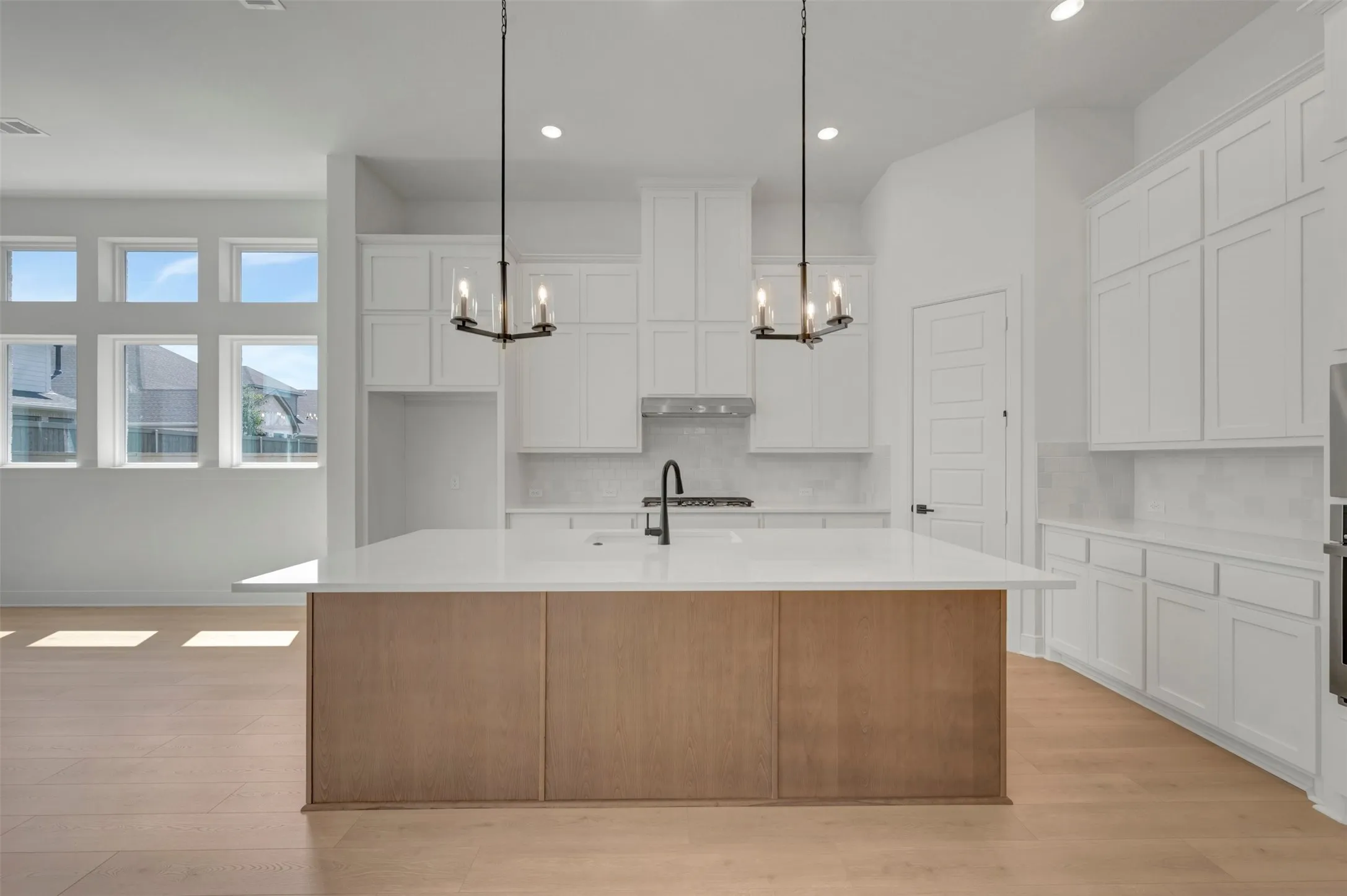 Open-concept kitchen featuring a large central island with a wood-finish base, white countertop, and contemporary black faucet