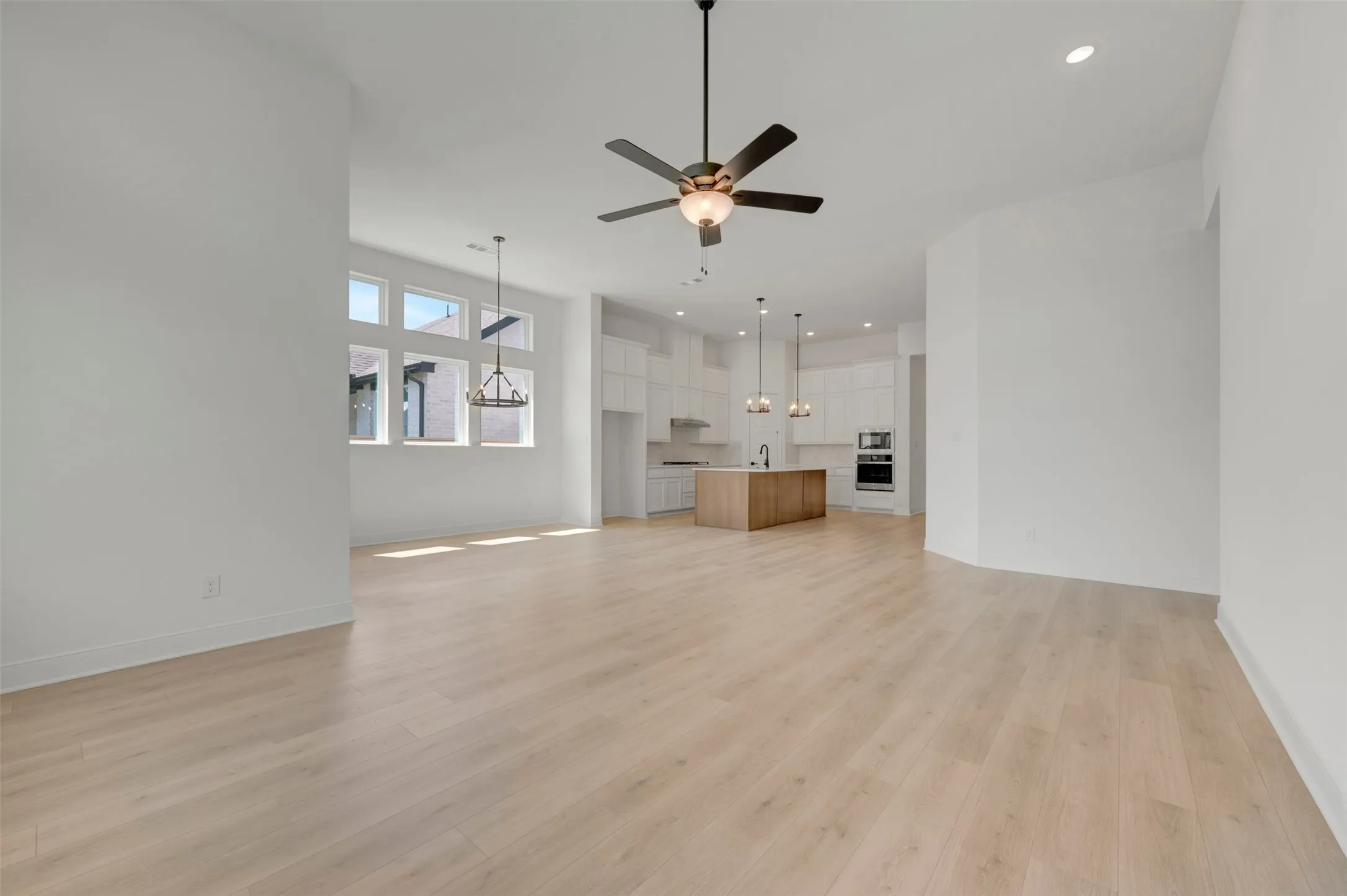 Expansive open-concept living area featuring light wood-finish flooring, a contemporary ceiling fan, and recessed lighting