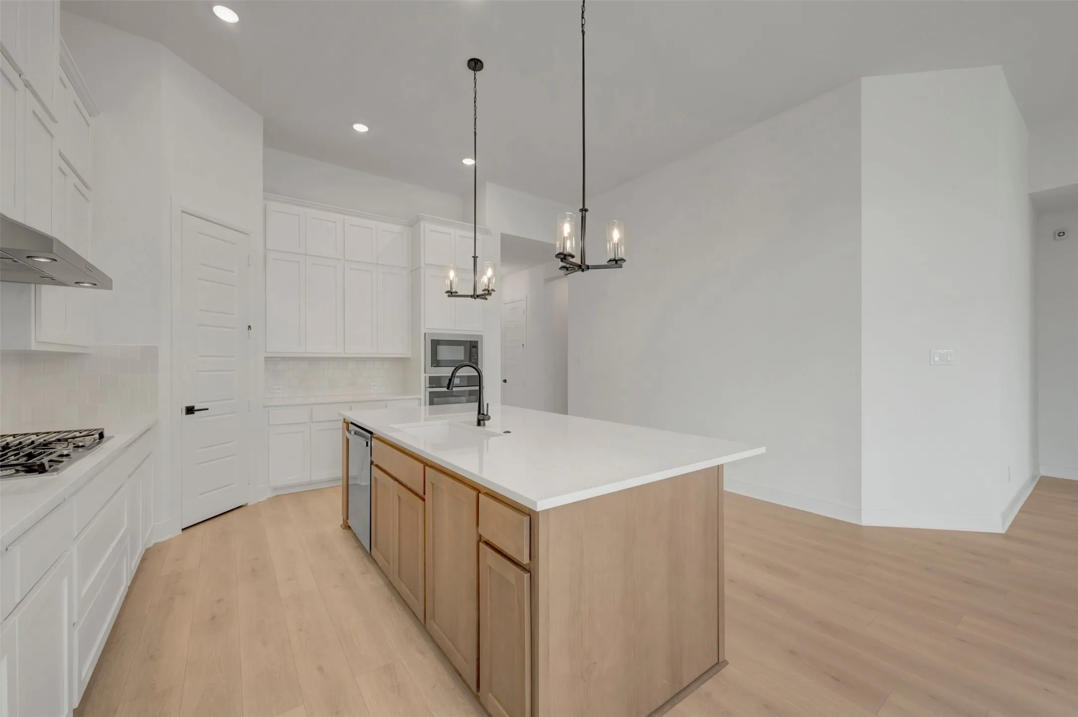 Modern kitchen featuring a light wood-finish flooring, white cabinetry, a large center island with a light-toned countertop, and recessed lighting