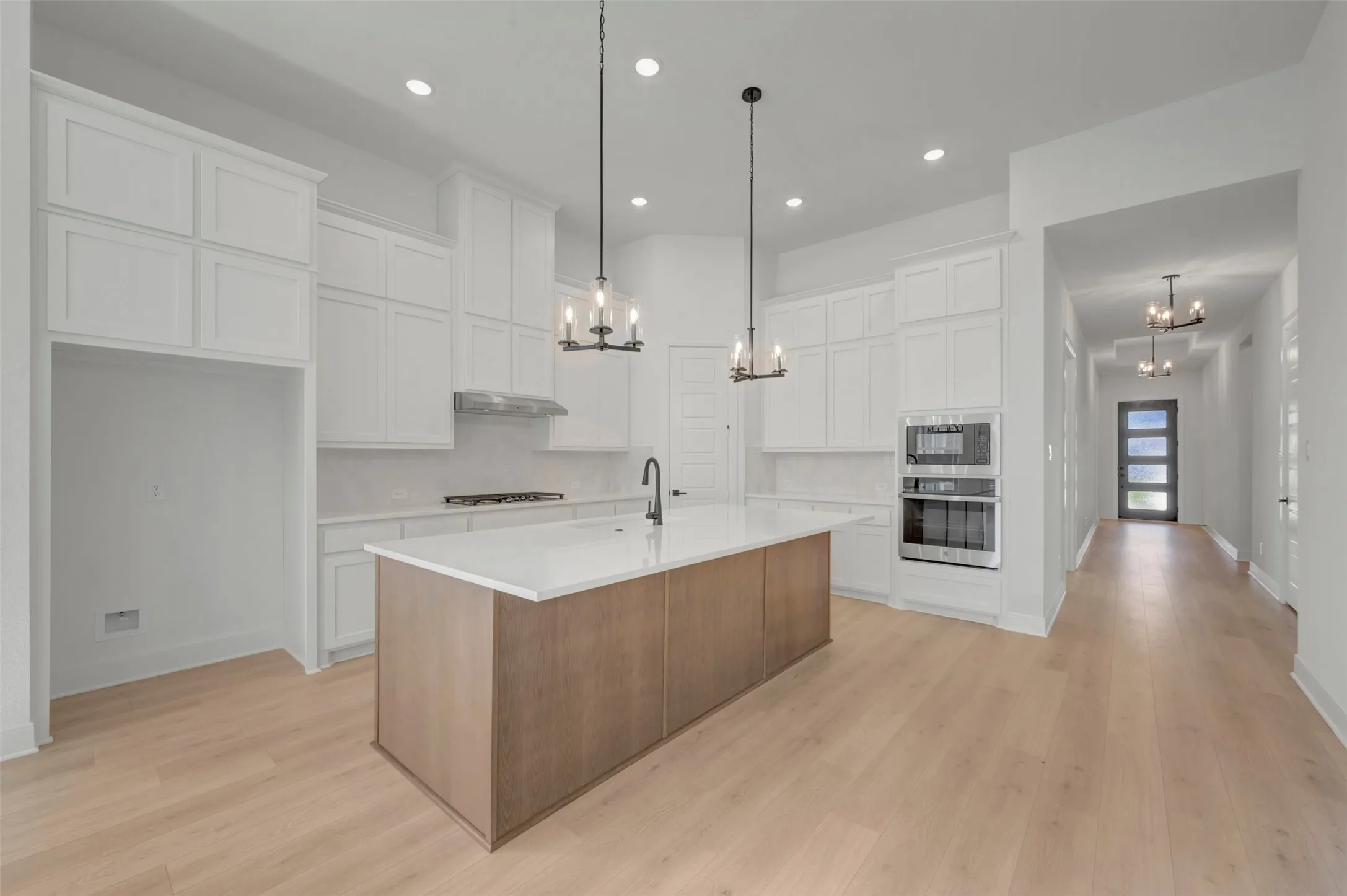 Modern kitchen featuring a large central island, light wood-finish flooring, white cabinetry, integrated double ovens, and recessed lighting