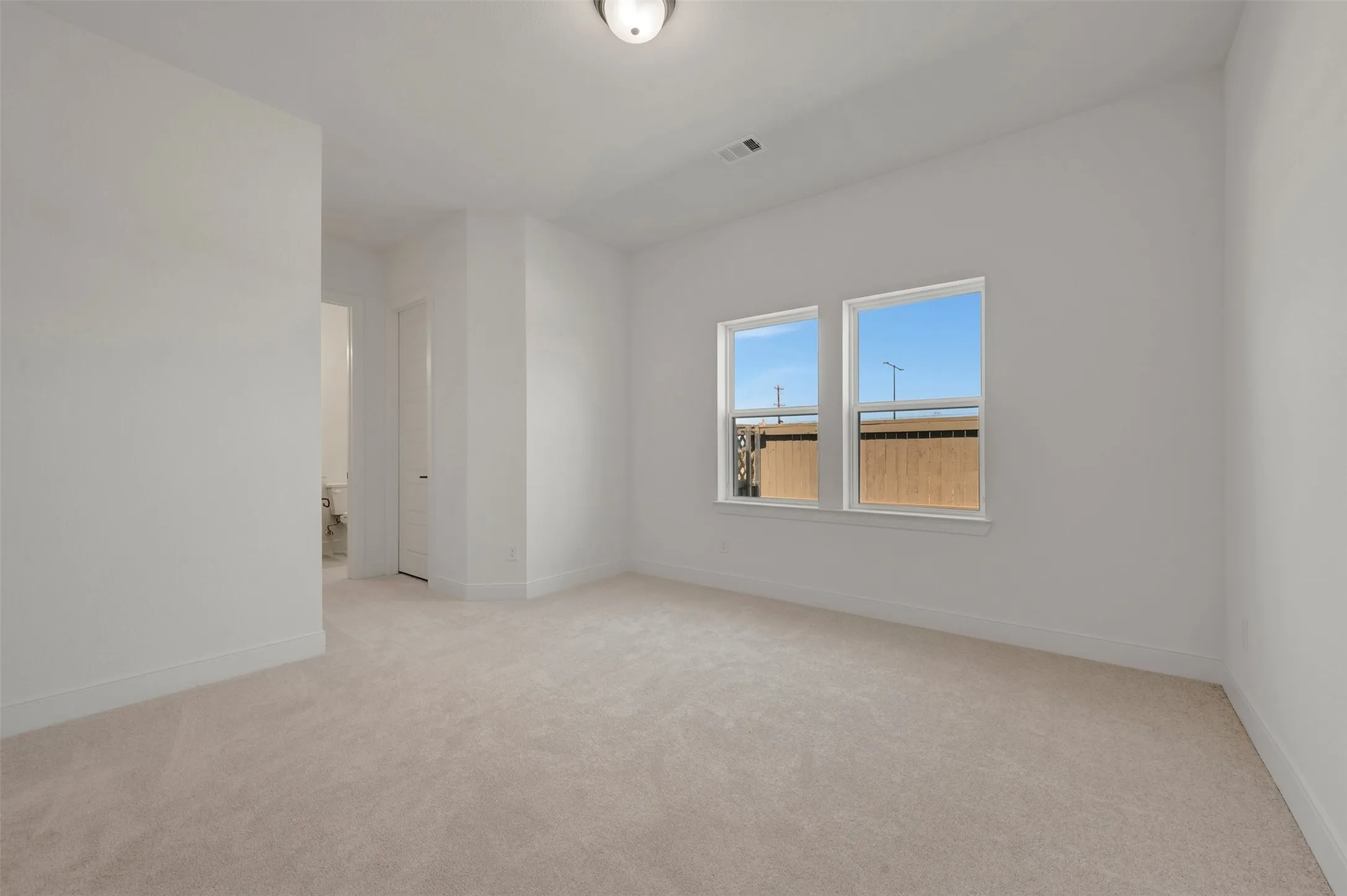 Spacious room featuring neutral carpeting, white baseboards, and two large windows