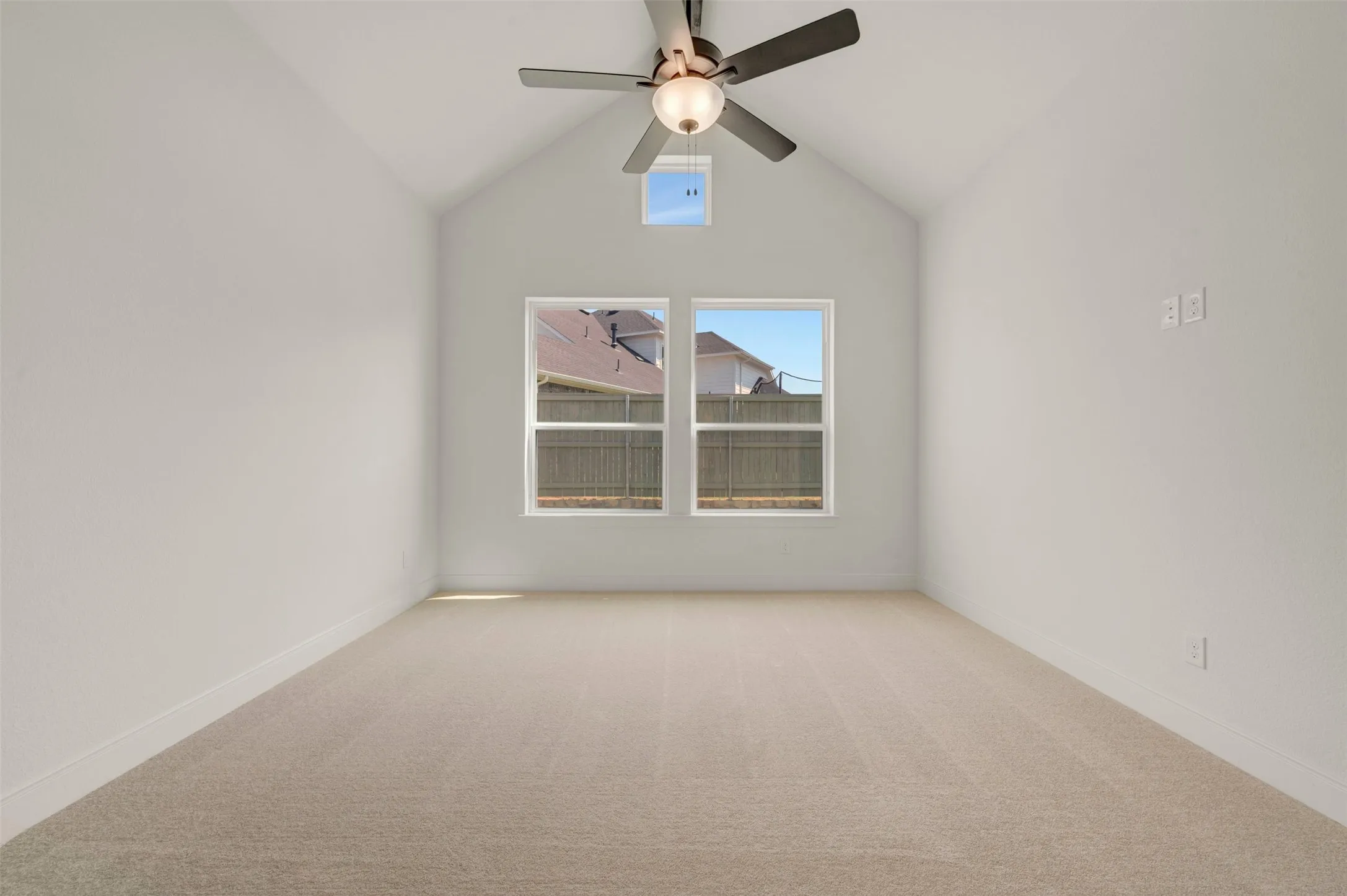 Room featuring a vaulted ceiling with a ceiling fan, two windows, and light-toned carpeting