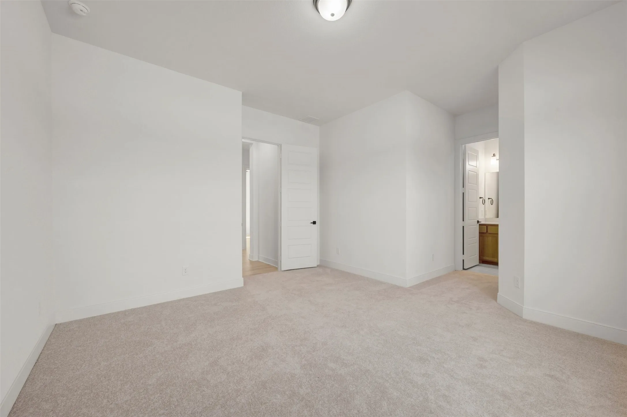 Spacious room featuring neutral carpeting, white walls, and bright overhead lighting