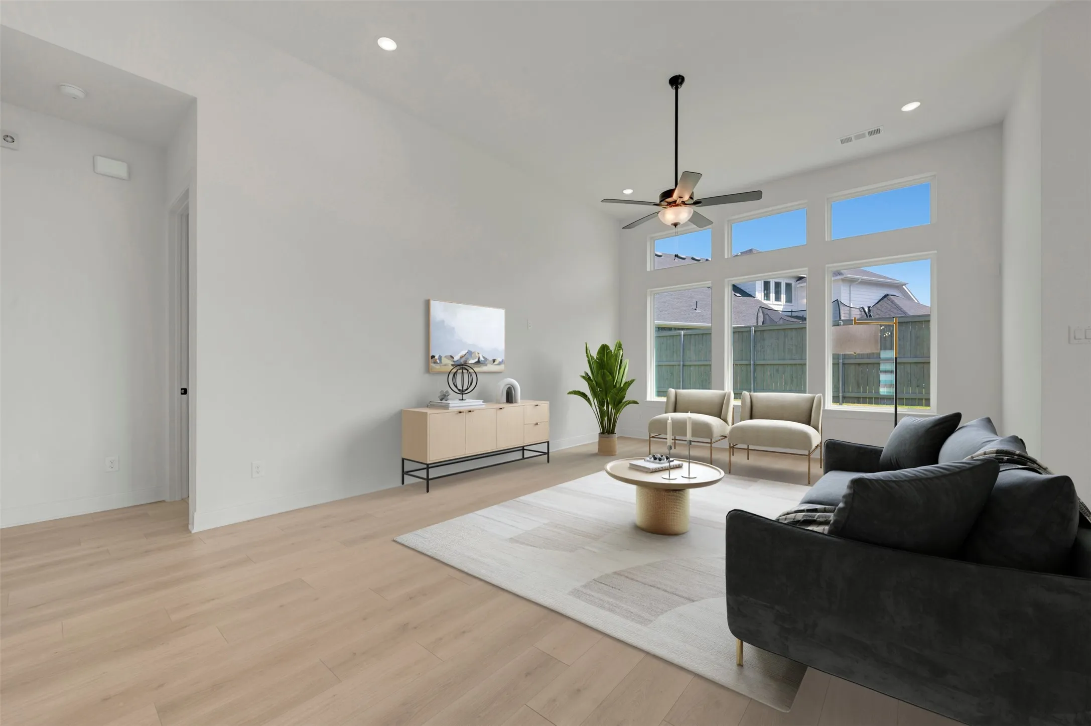 Vaulted ceiling living area featuring wood-finish flooring, a contemporary ceiling fan, recessed lighting, and a wall of transom windows